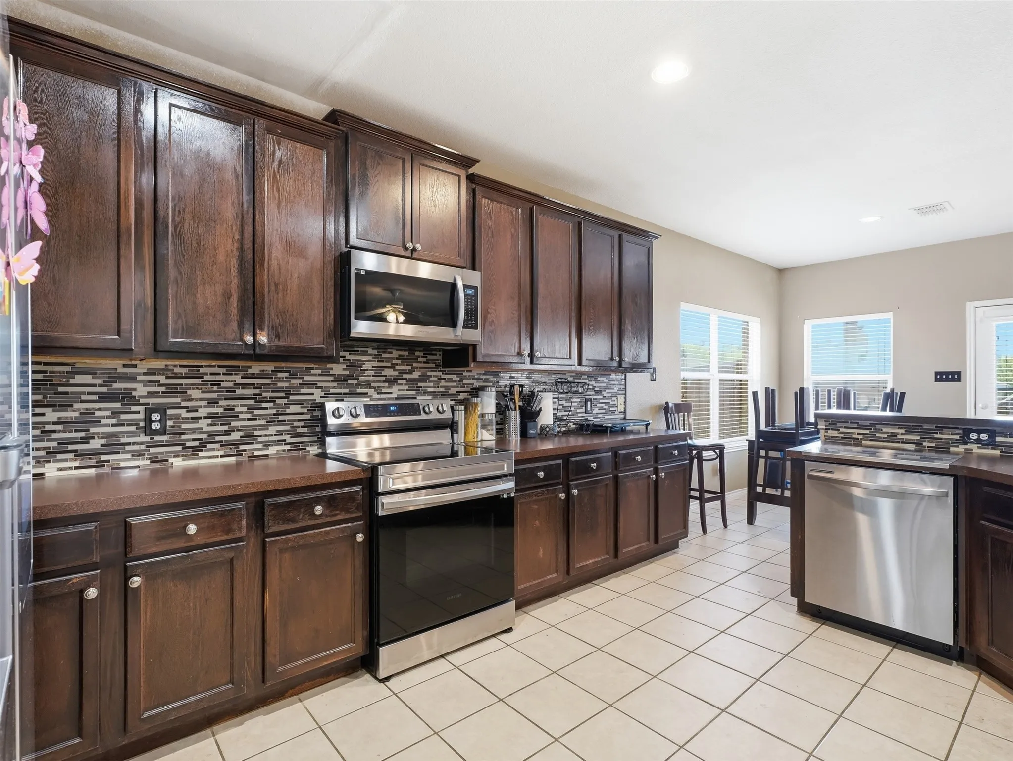 Expansive kitchen featuring dark wood cabinetry, stainless steel appliances, a mosaic tile backsplash, and light tile flooring