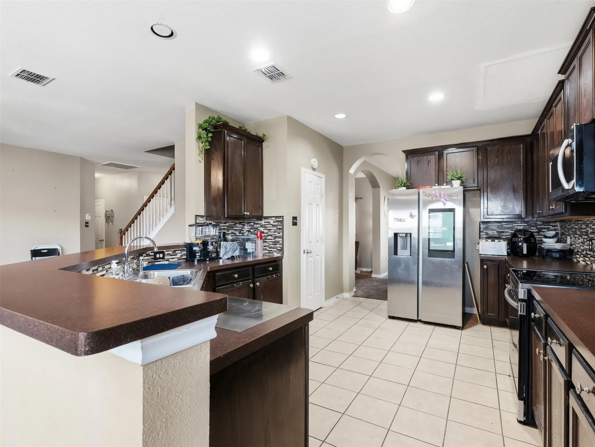 Kitchen featuring dark wood cabinetry, a mosaic tile backsplash, solid surface countertops, tile flooring, and a stainless steel side-by-side refrigerator