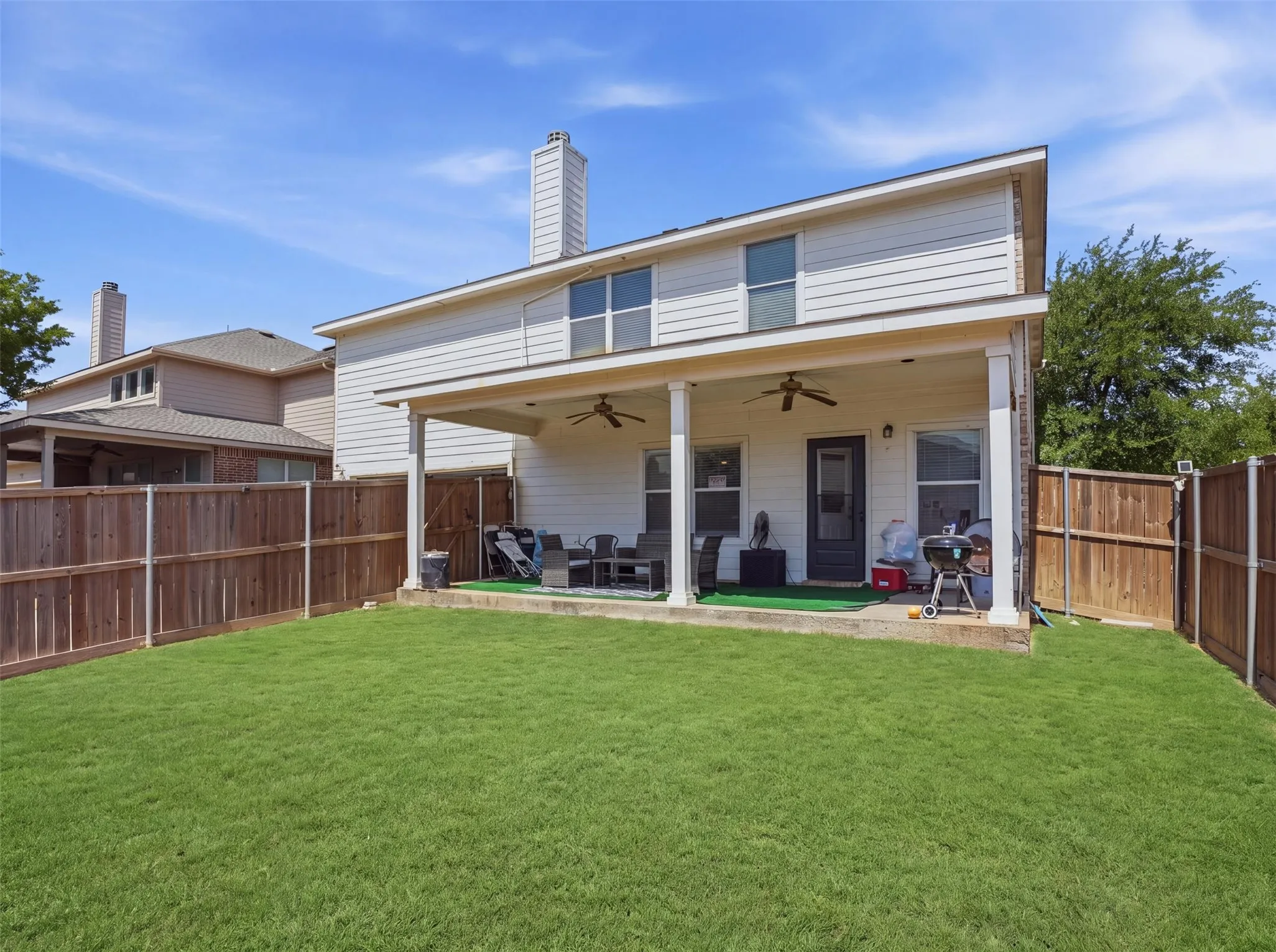 Expansive backyard featuring a covered patio with ceiling fans, a manicured lawn, and wood privacy fencing