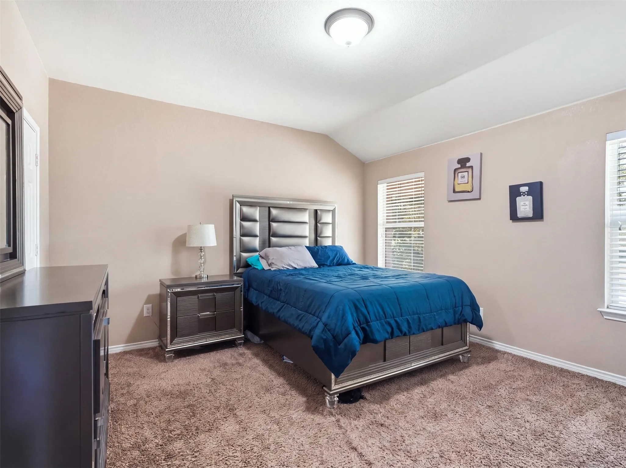 Vaulted ceiling, ceiling-mounted light fixture, two windows with blinds, and textured wall finish