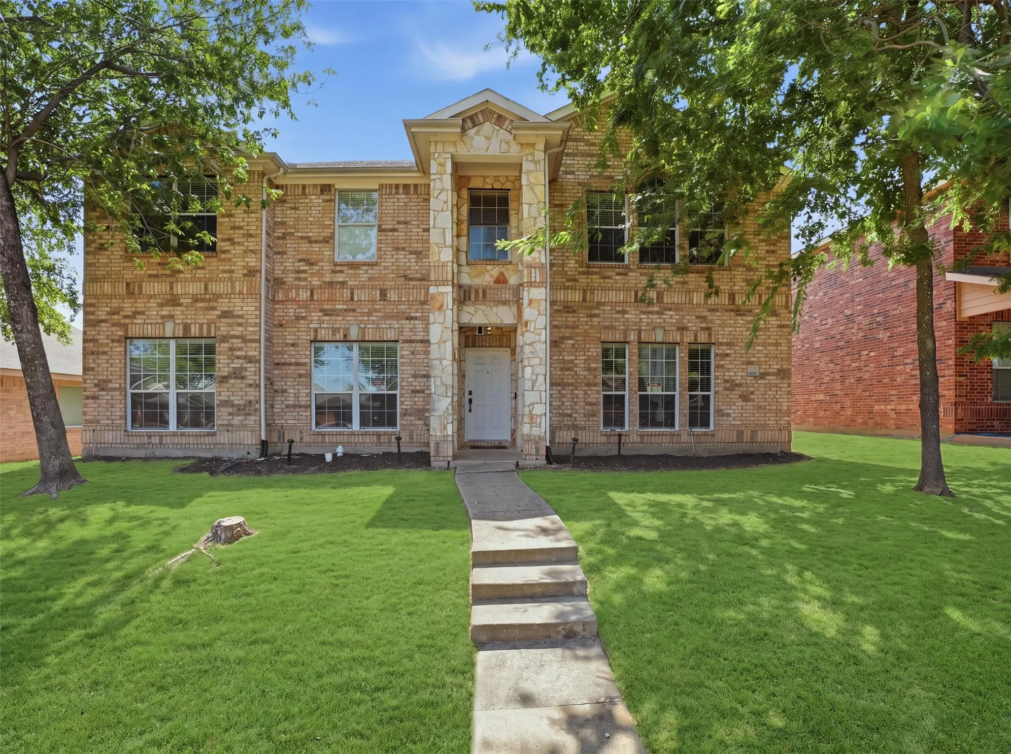Brick and stone façade with multiple windows, concrete walkway, and a manicured lawn