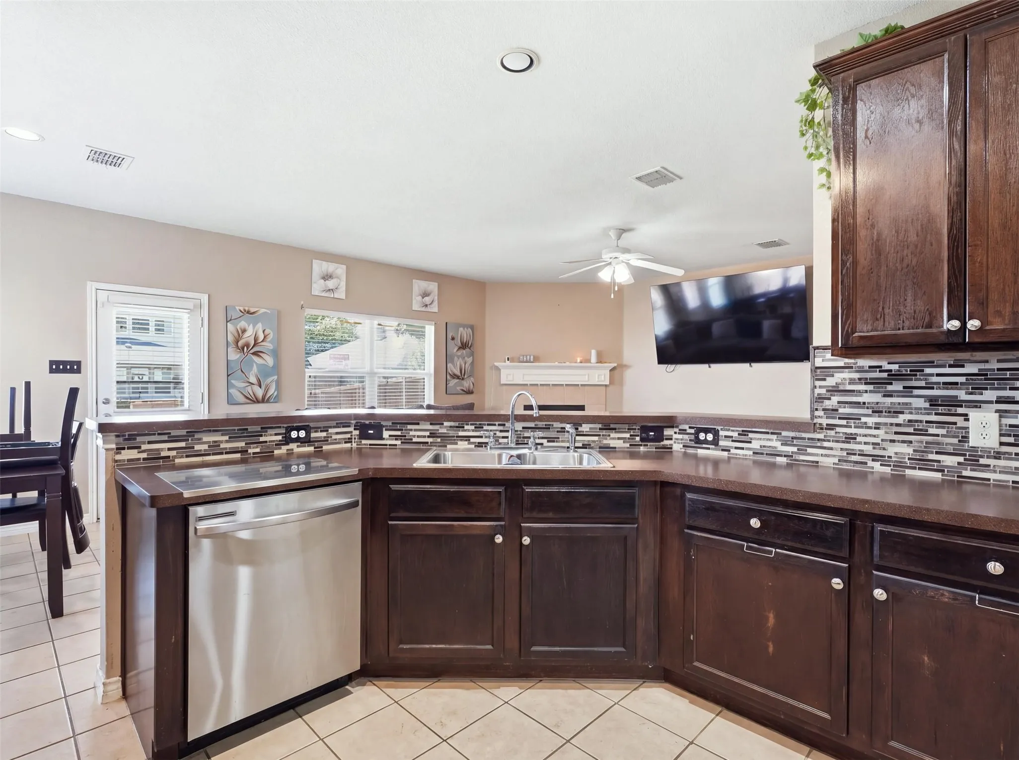 Kitchen featuring dark wood cabinetry, a stainless steel dishwasher, and a tile backsplash with mosaic accents