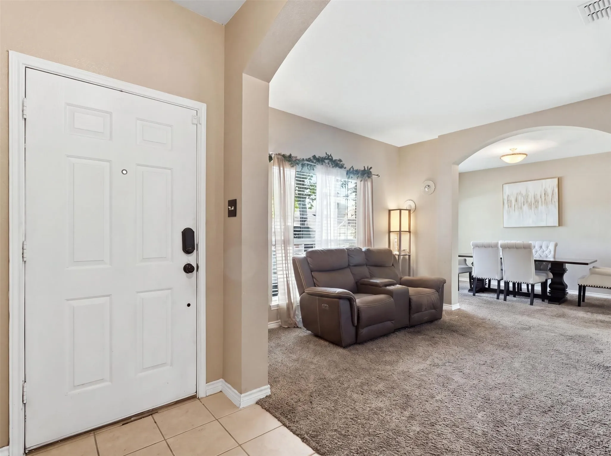 Entryway with tiled flooring, leading to a carpeted living space with a large window