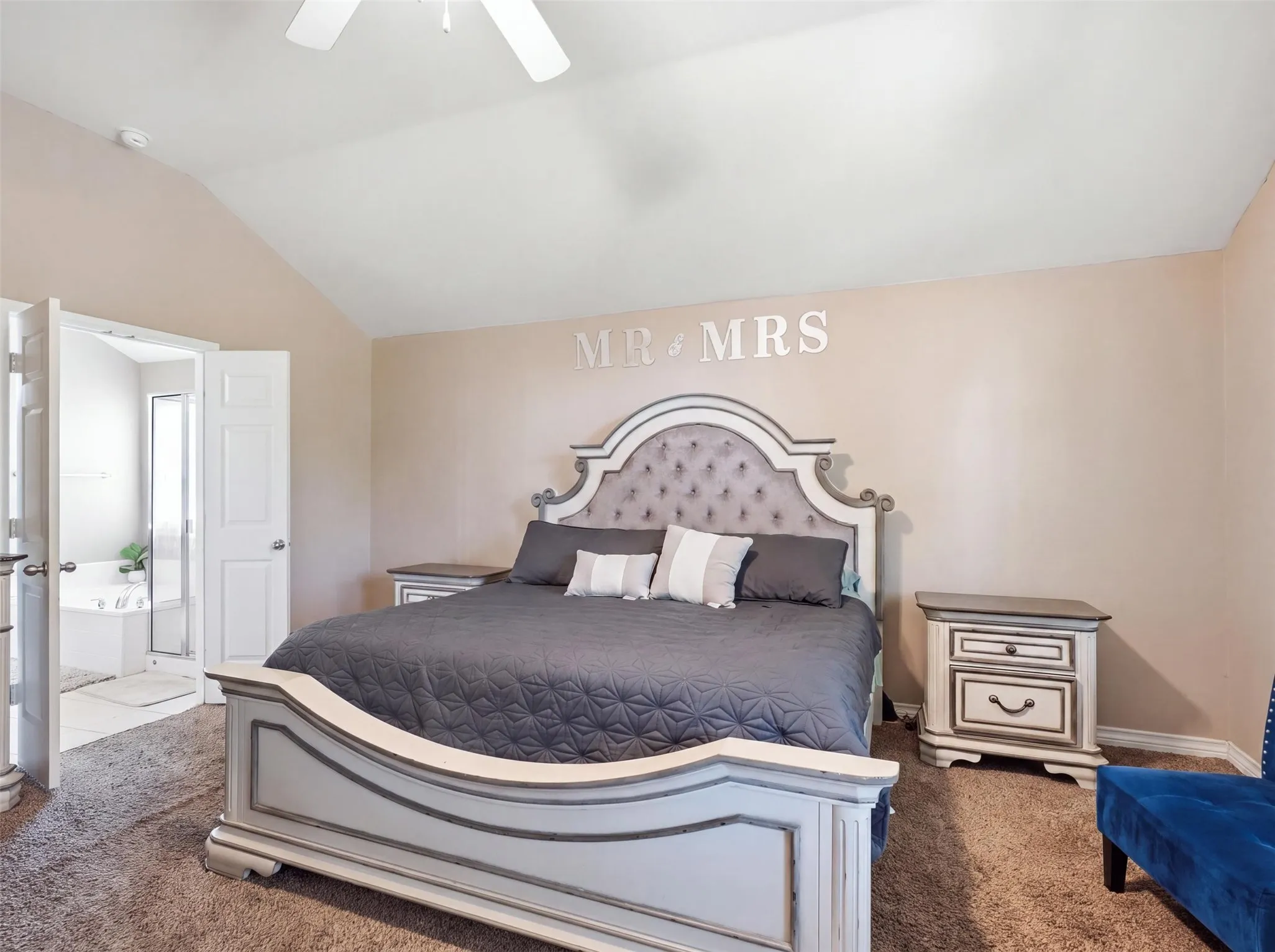 Vaulted ceiling with a ceiling fan, carpeted flooring, and an adjoining bathroom featuring a jetted tub