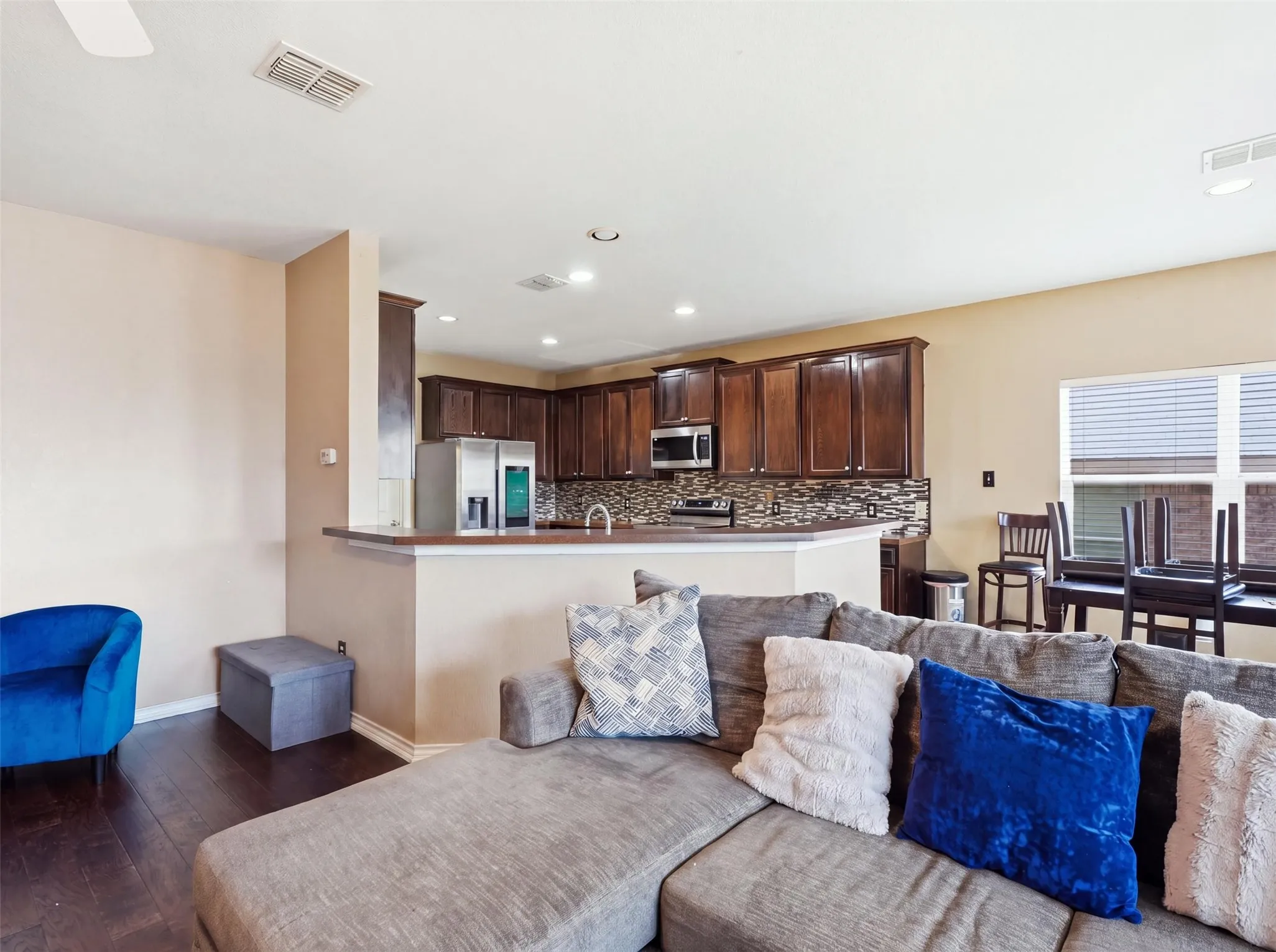 Wood-finish flooring throughout, kitchen with dark wood cabinetry, stainless steel appliances, and a mosaic tile backsplash