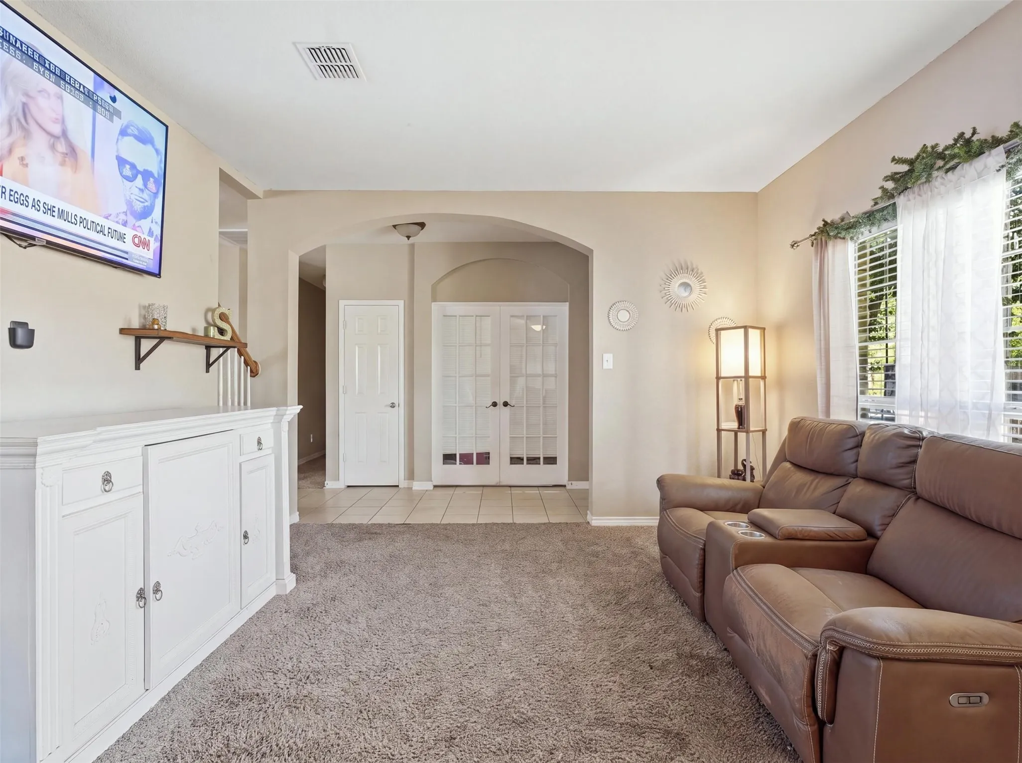 Neutral wall color, arched doorways, tiled flooring, French doors, and windows with white blinds