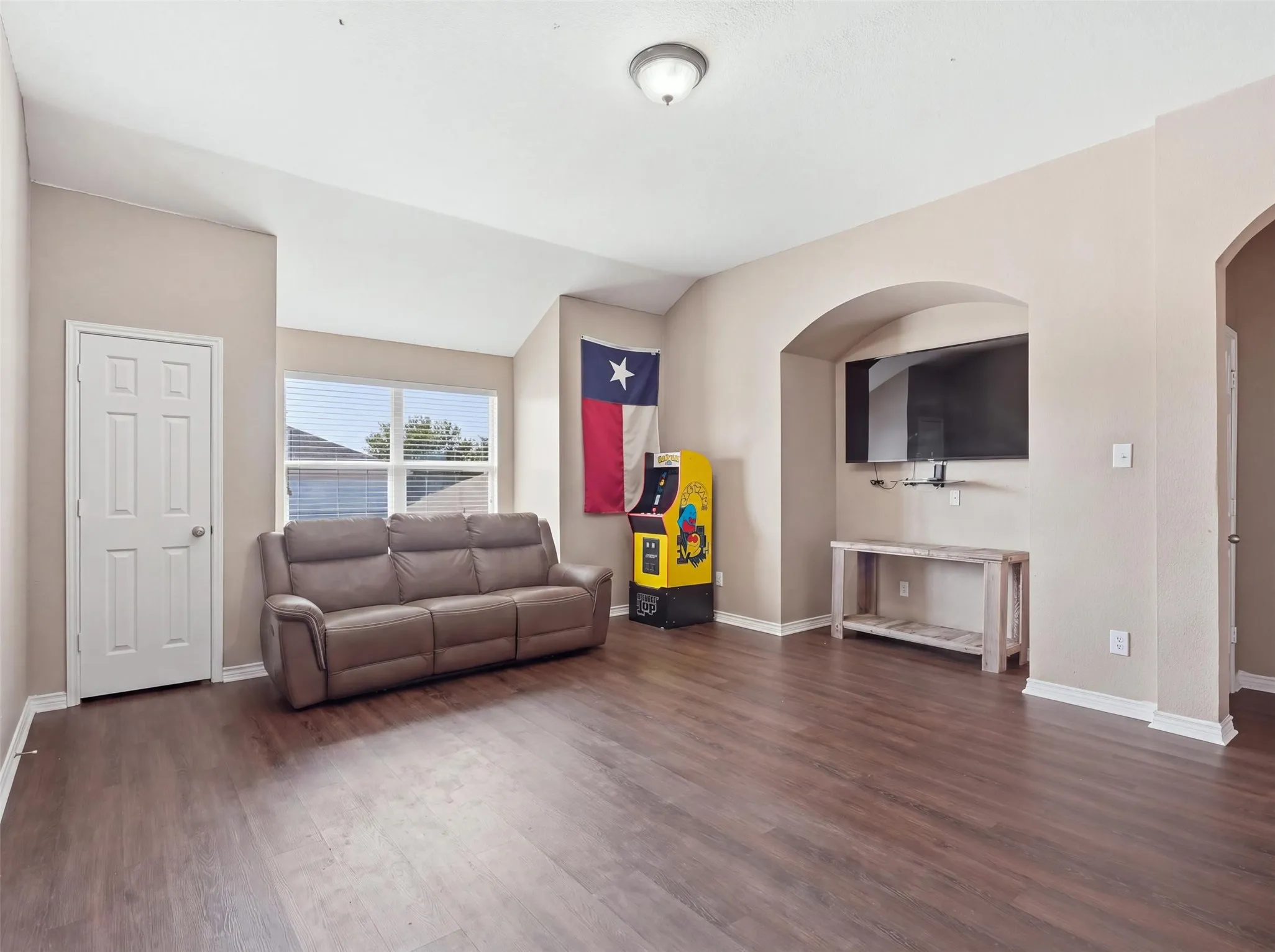 Vaulted ceiling with a flush mount light fixture, wood-finish flooring, and a large window with blinds