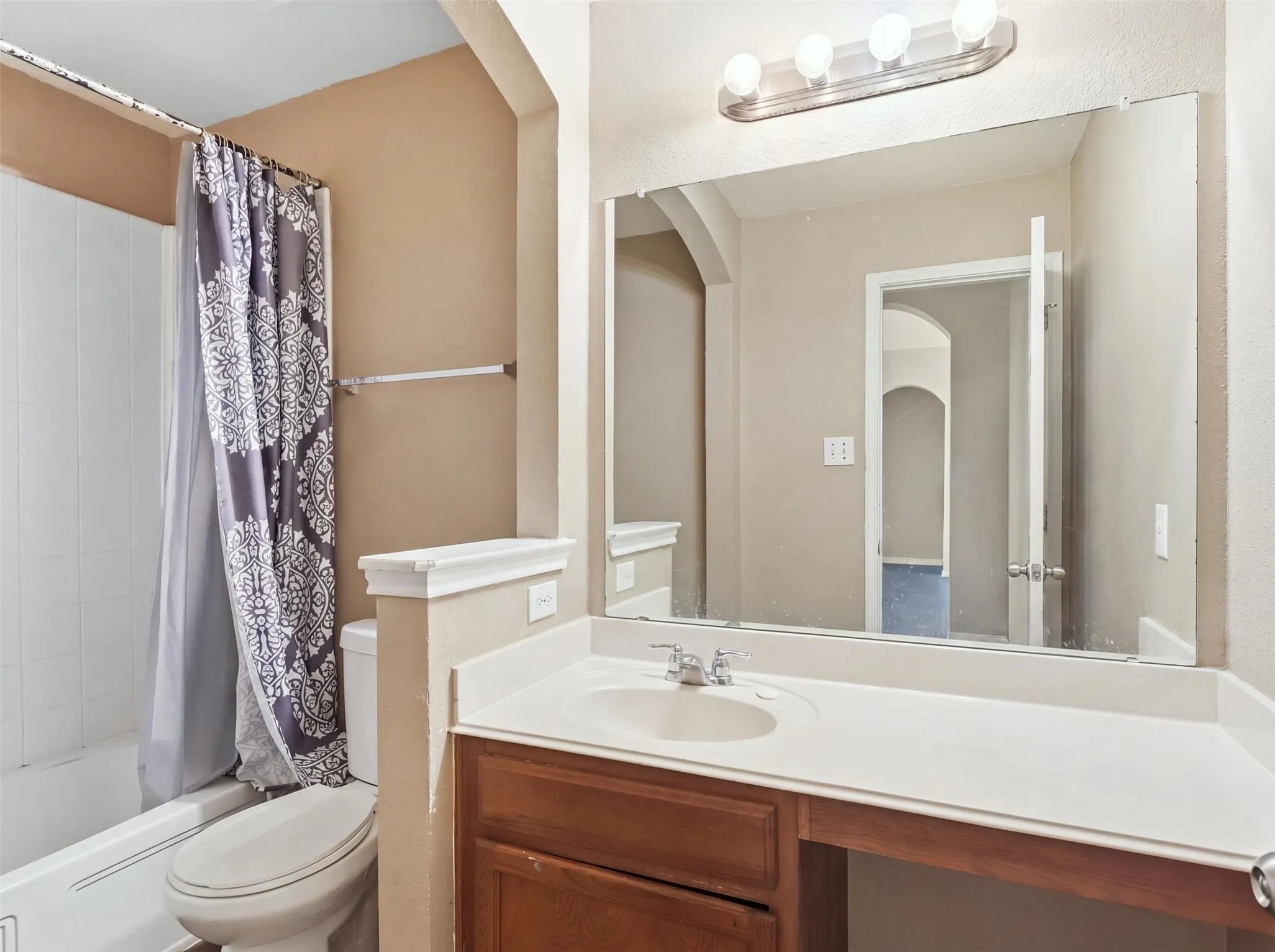 Vanity with integrated sink and chrome faucet, wood-finish cabinetry, full-width mirror, and a three-bulb vanity light fixture
