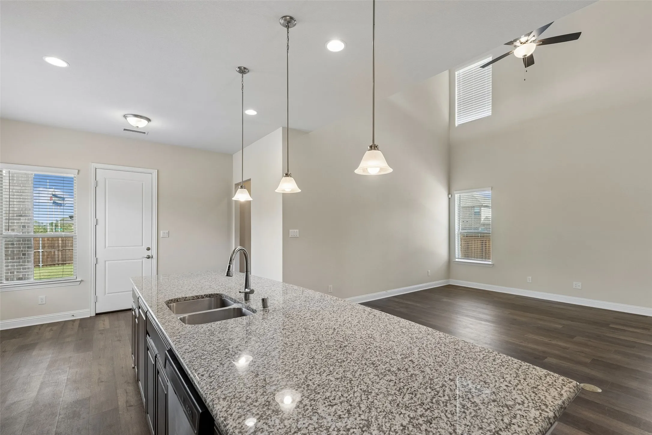 View of the kitchen, living room and eat in kitchen area. Featuring LVP flooring, plenty of natural light, deep sink and extended granite island. Door leads to back porch.