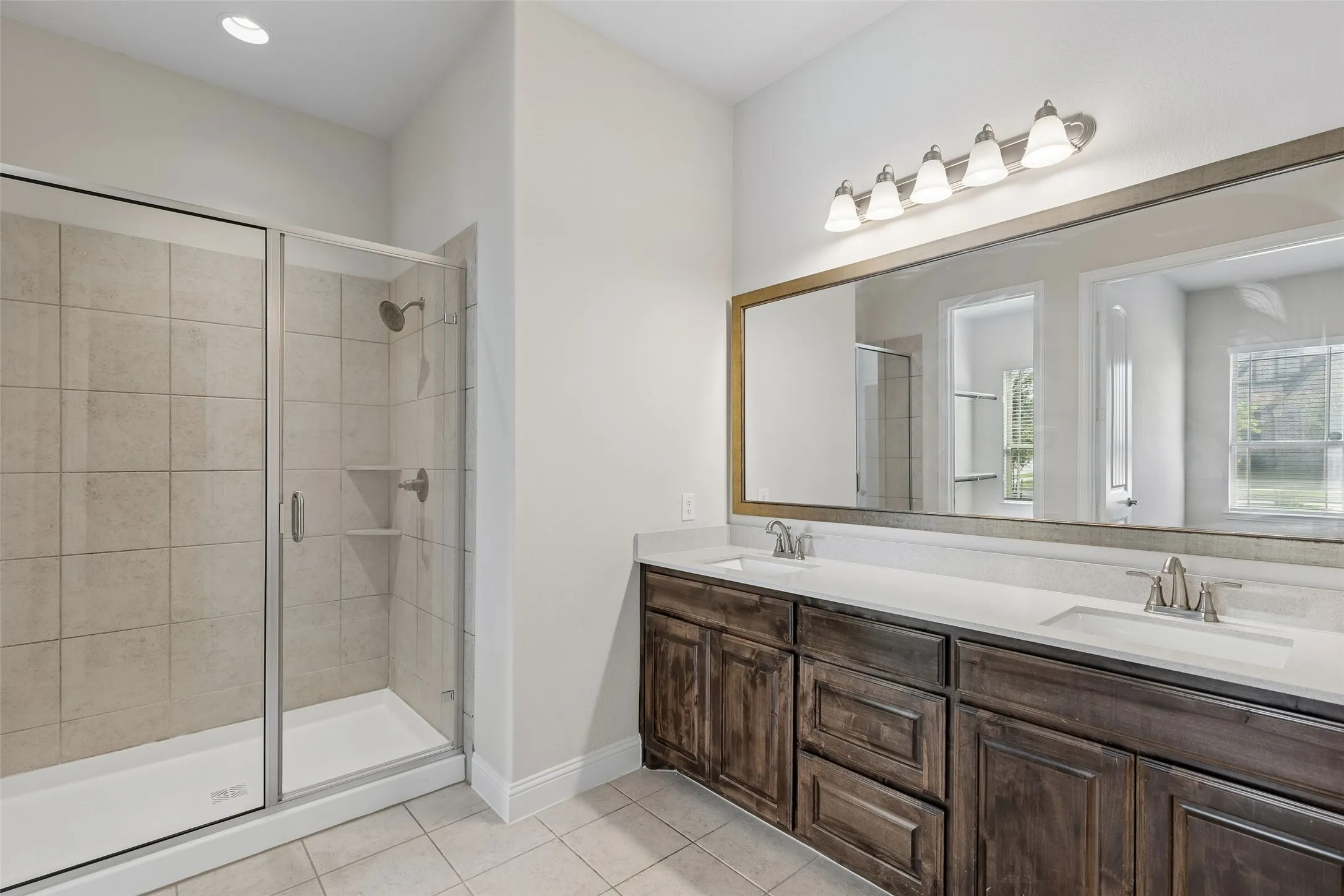Primary bathroom featuring a walk in shower, tile flooring, cabinetry and double sinks.