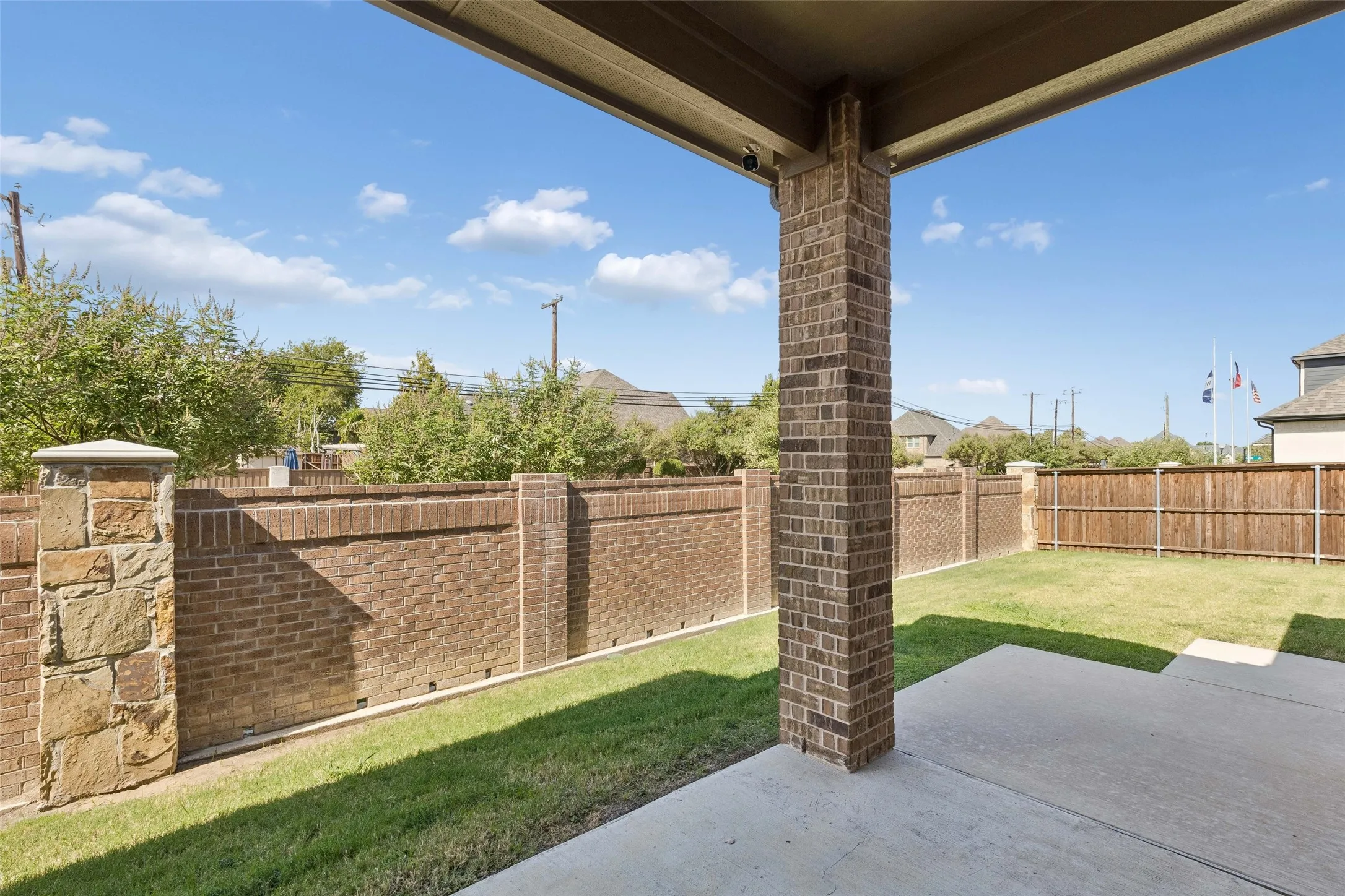 Back patio featuring no neighbors to the right or to the left, a stone and brick wall fence, wood fence and a concrete path out to the driveway.