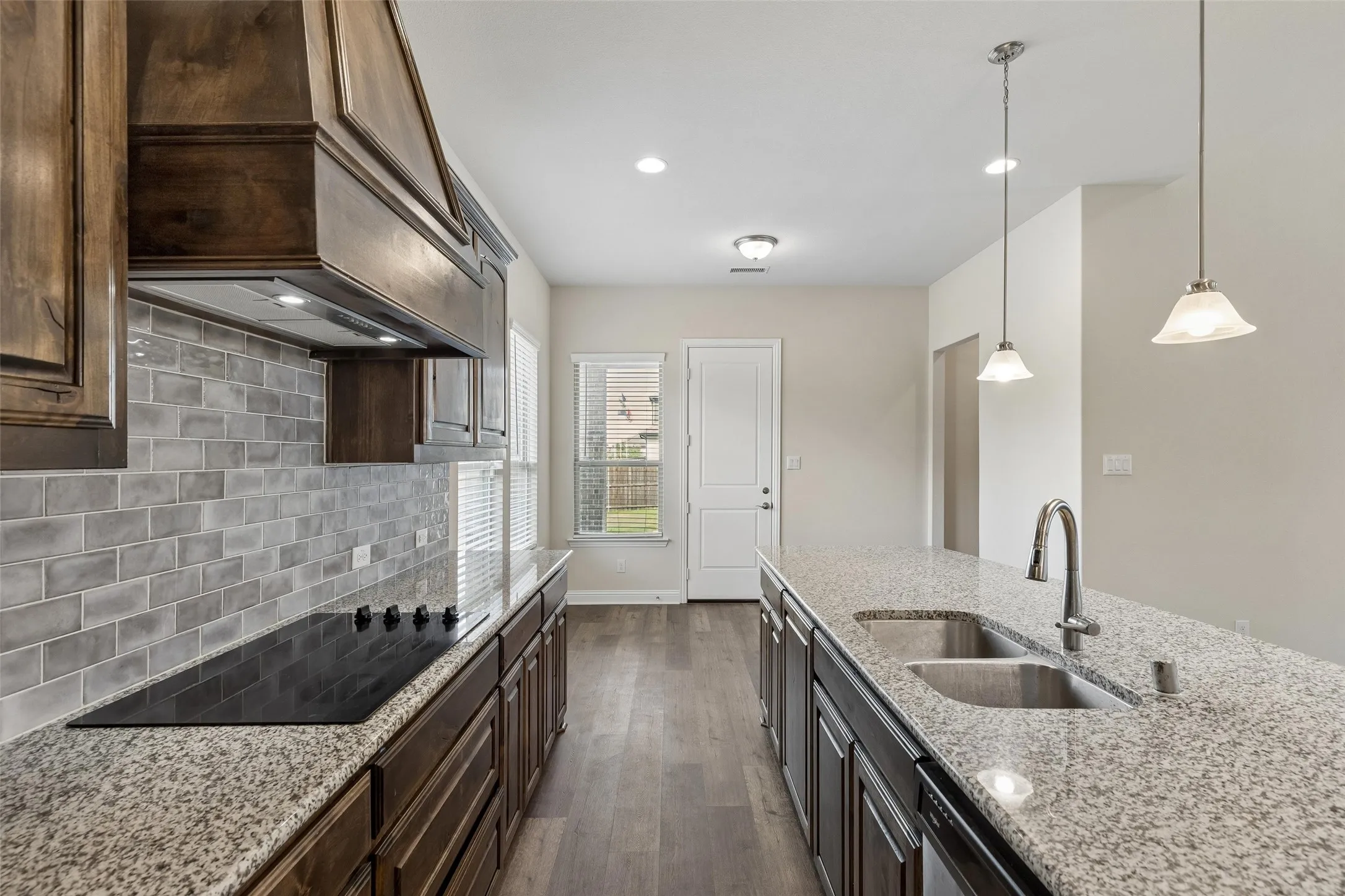 View of the kitchen. Featuring LVP flooring, plenty of natural light, range hood, glass top stove, dishwasher, deep sink, extended cabinets and extended granite island.