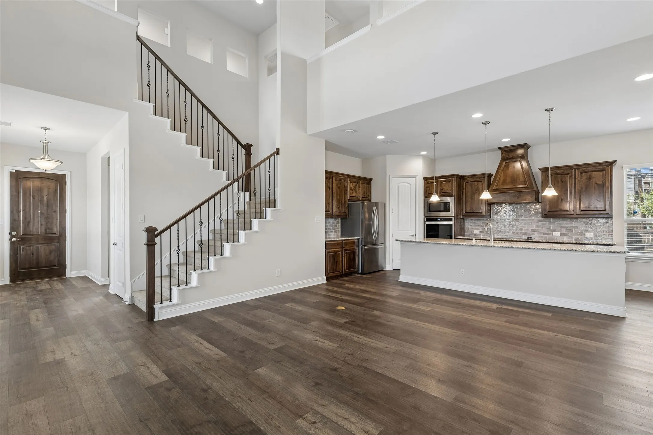 View of the front door, foyer, living room and kitchen. Featuring LVP flooring, high ceilings and a beautiful wood front door.