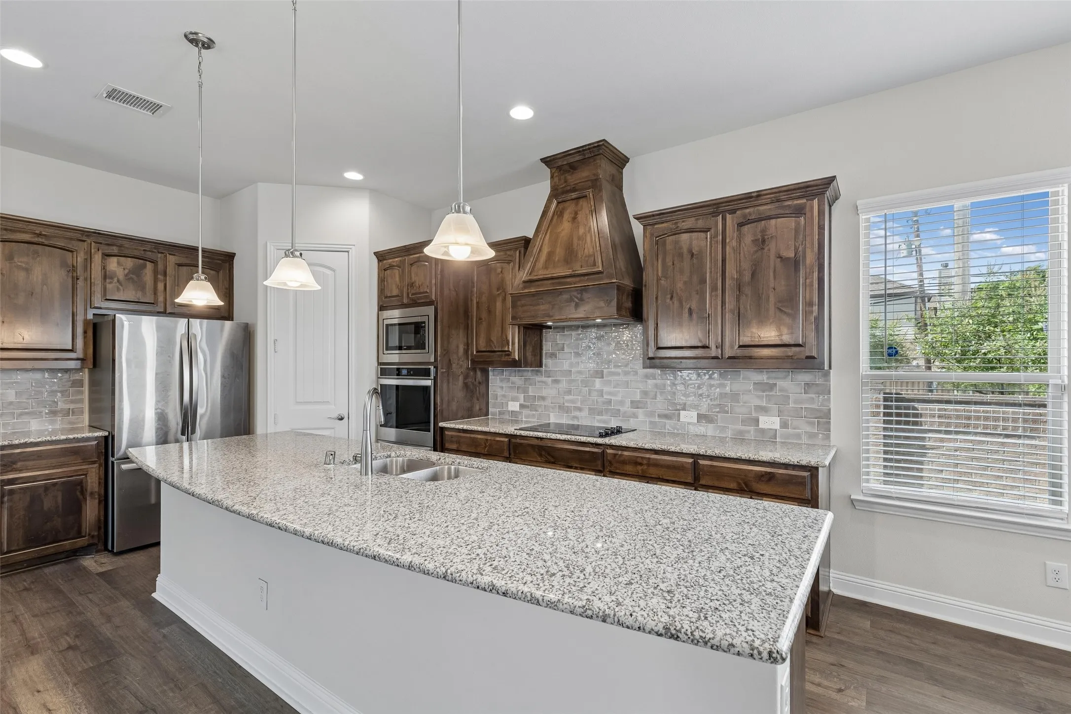 View of the kitchen. Featuring LVP flooring, plenty of natural light, range hood, glass top stove, double oven, extended cabinets and extended granite island.