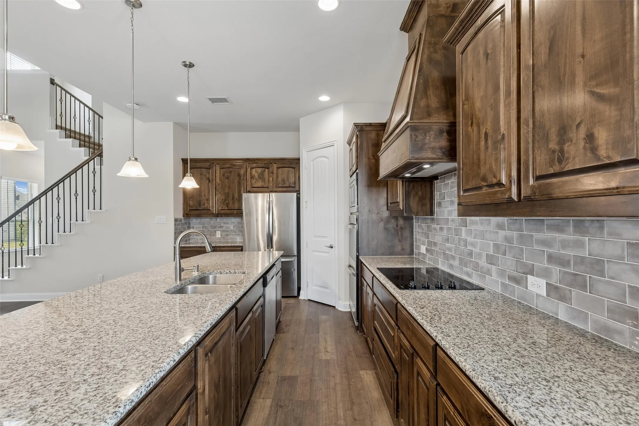 View of the kitchen. Featuring LVP flooring, plenty of natural light, range hood, glass top stove, double oven, dishwasher, deep sink, extended cabinets and extended granite island.
