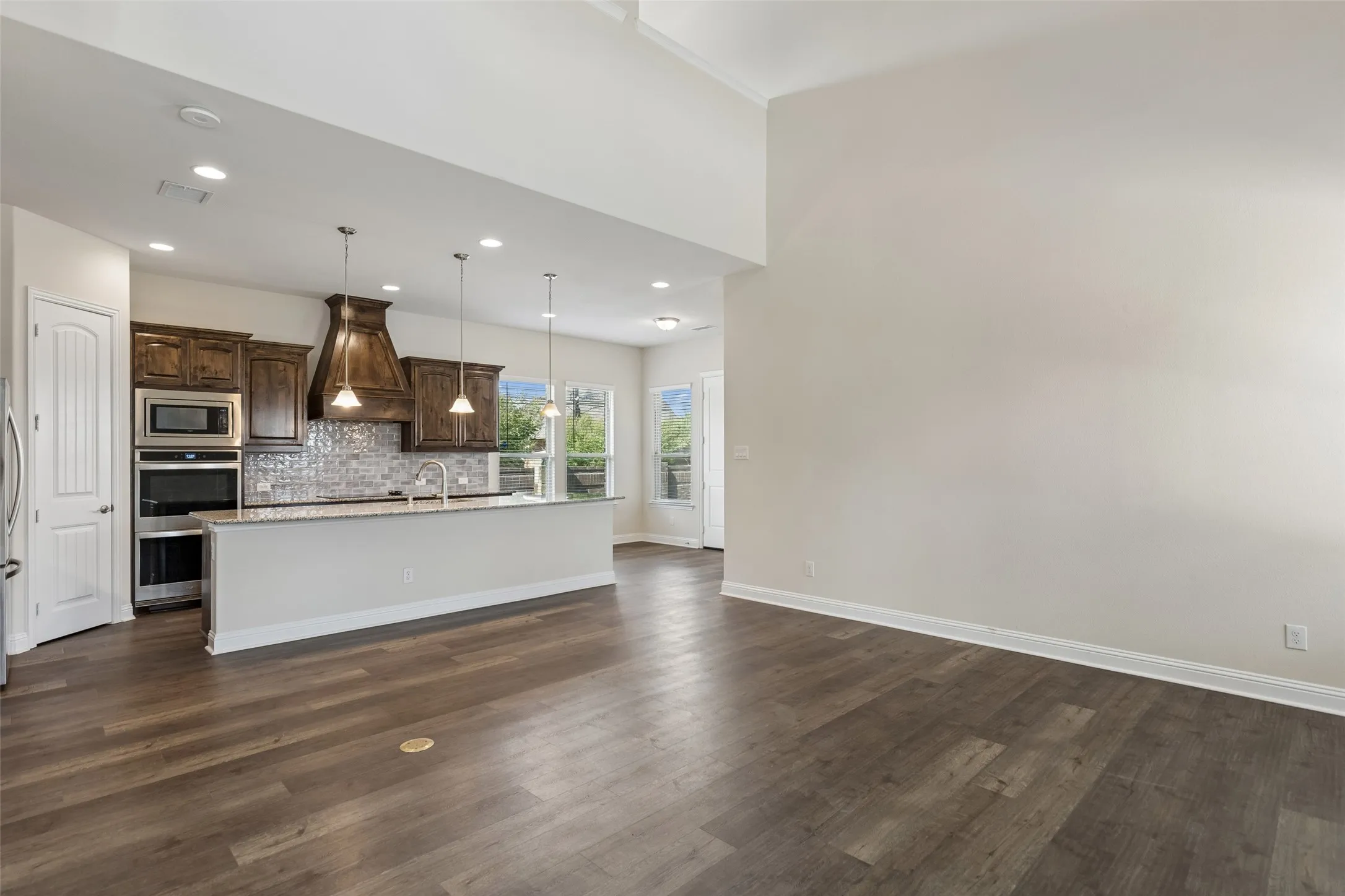 View of the living room, kitchen and the eat in kitchen area. Featuring LVP flooring, the brass outlet in the living room floor, plenty of natural light, range hood, double oven, extended cabinets and extended island.