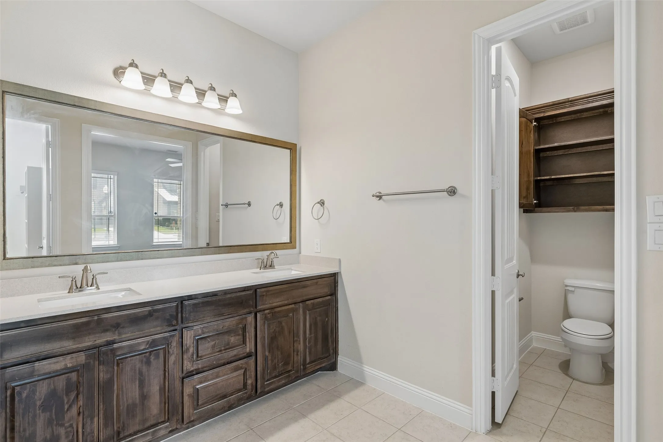 Primary bathroom featuring a walk in shower, tile flooring, cabinetry and double sinks.