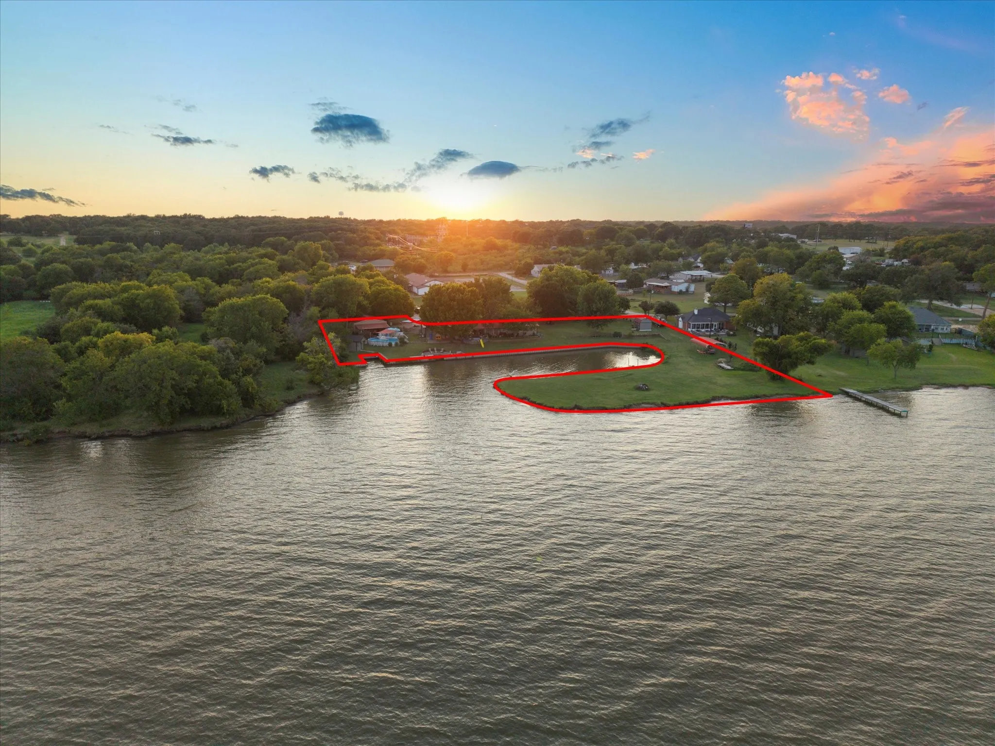 Waterfront property featuring a private dock, expansive grassy areas, mature trees, and a tranquil pond