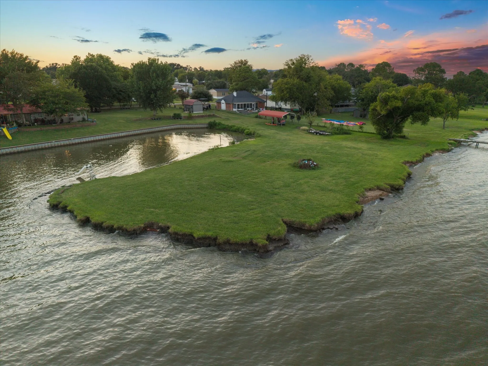 Waterfront property featuring a private canal, lush green lawn, and mature trees