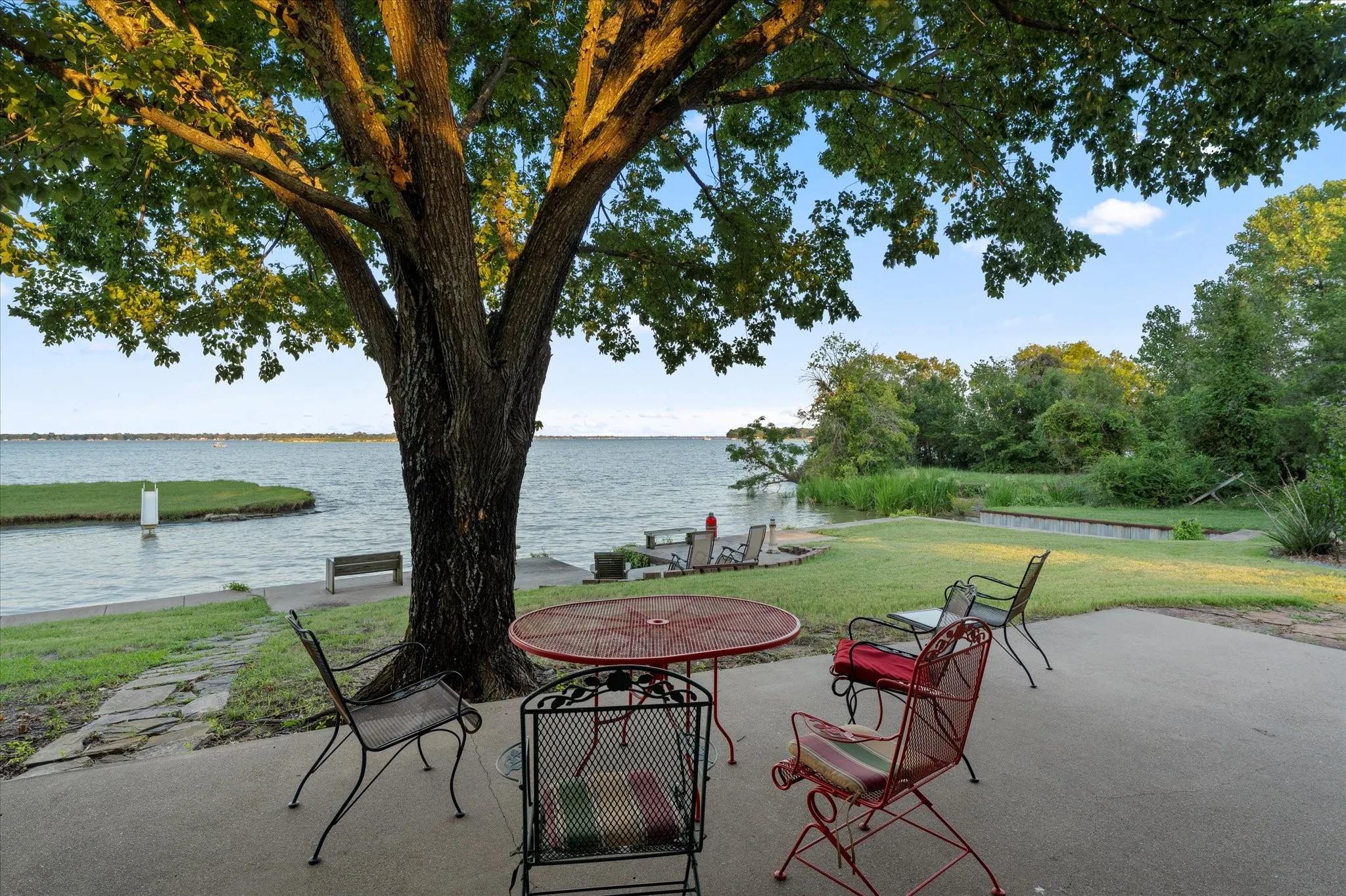 Expansive waterfront property featuring a concrete patio, mature trees, and a grassy area with natural landscaping