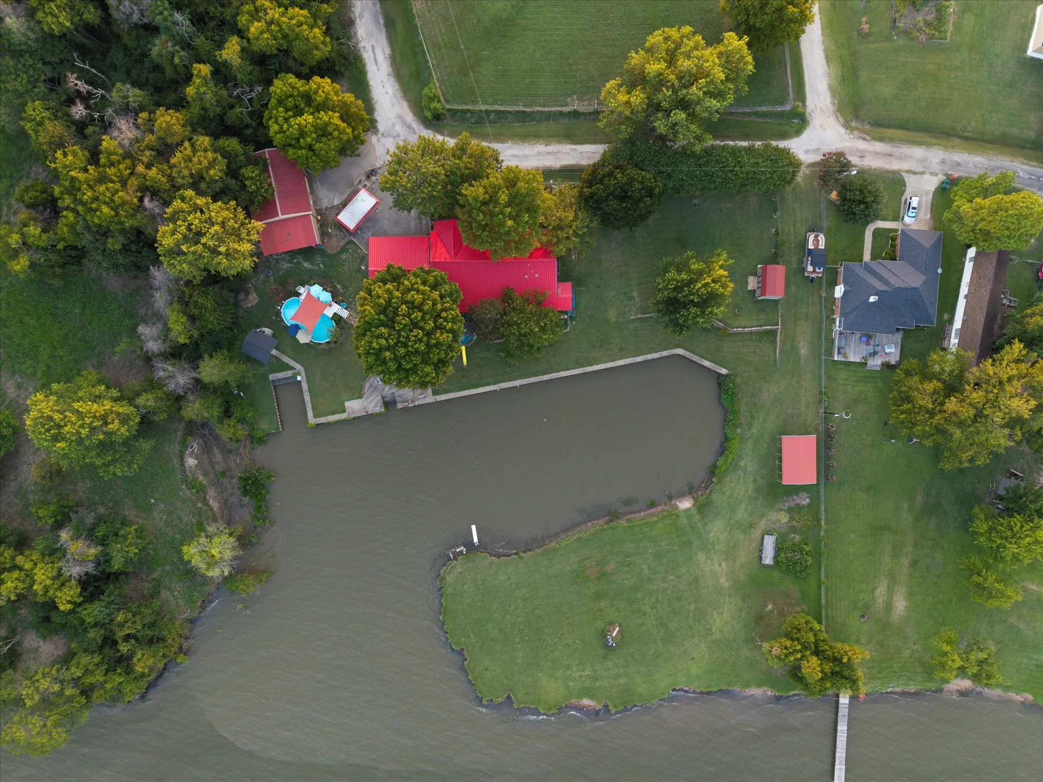 Waterfront property with a private pond, main residence featuring a red roof, and an additional structure with a red roof