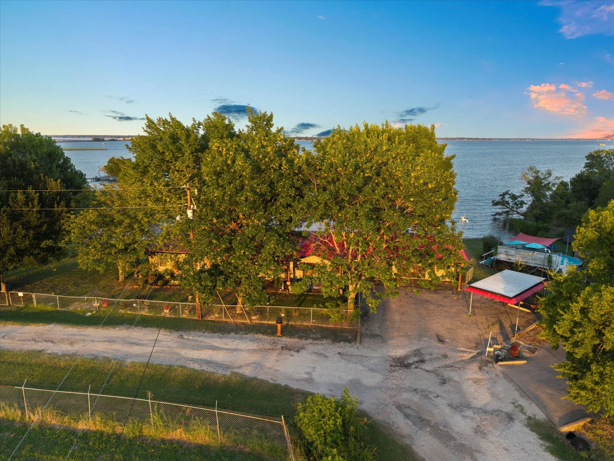 Waterfront property with mature trees, fenced perimeter, and a detached covered structure