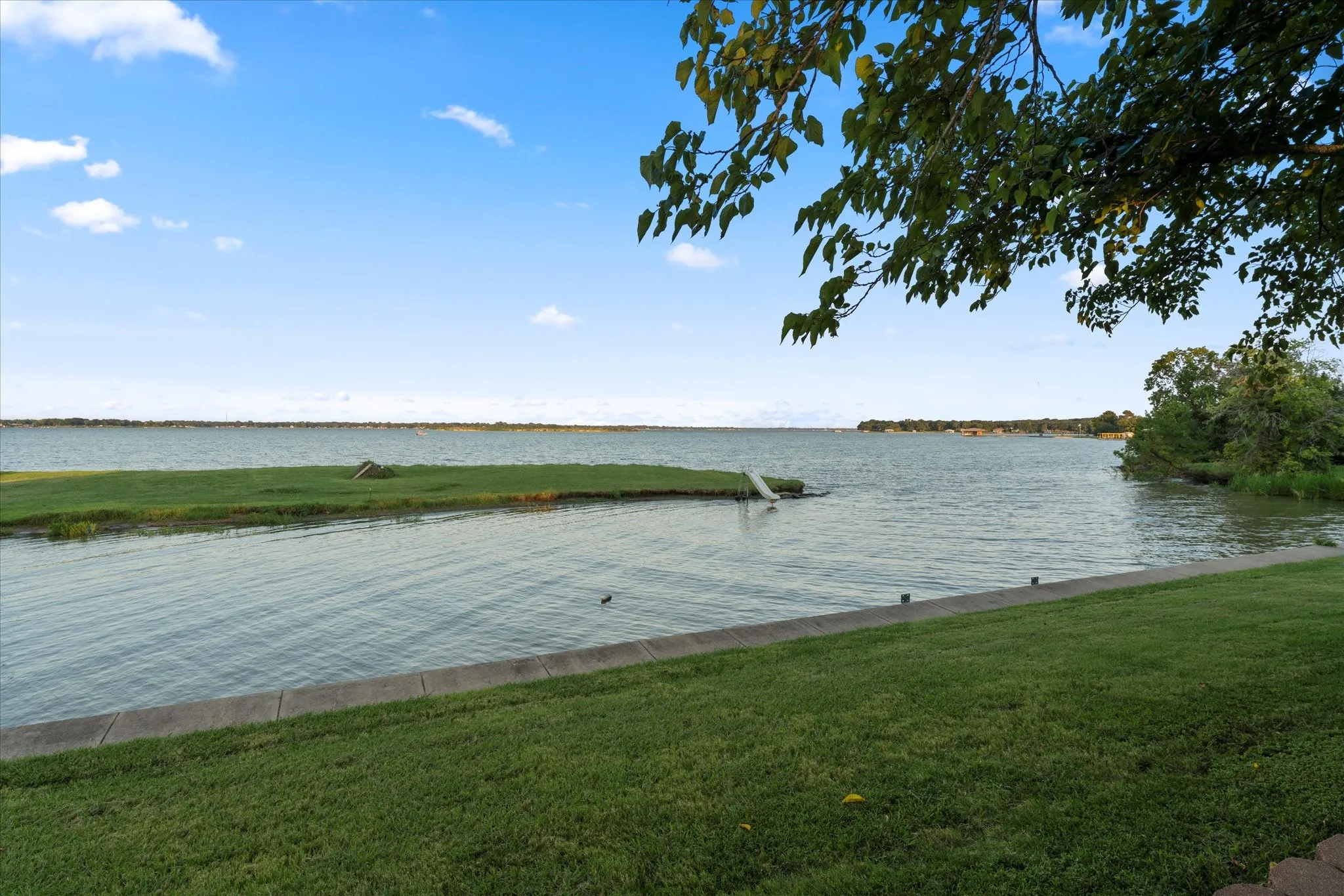 Waterfront property featuring a concrete retaining wall, a grassy lawn, and mature trees