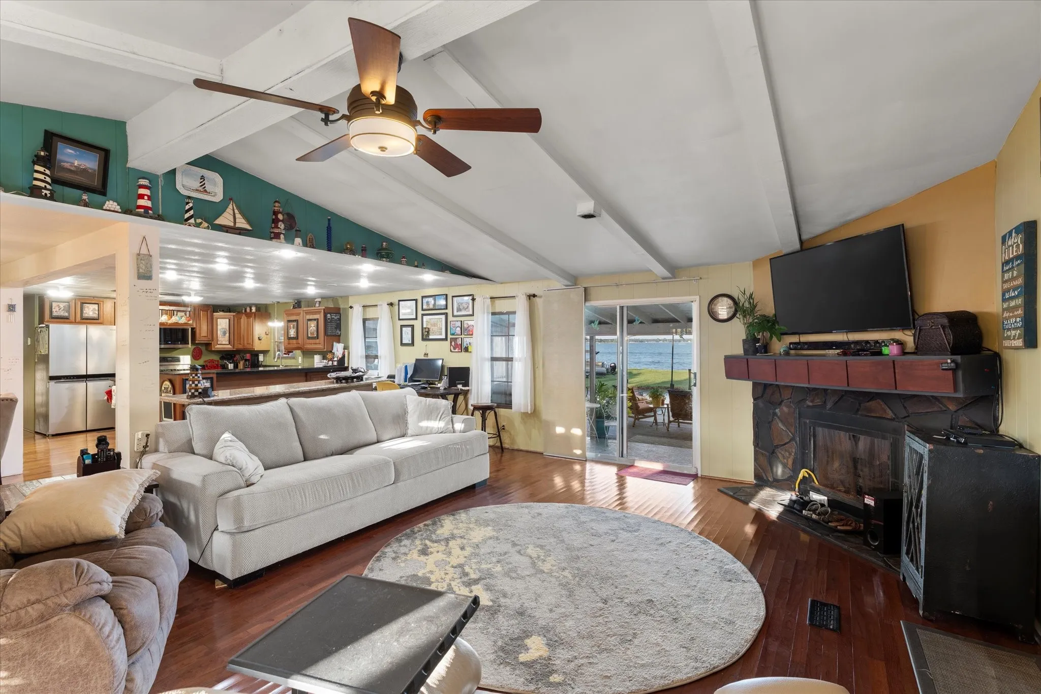 Vaulted ceiling with exposed beams, wood-finish flooring, stone-faced fireplace, and sliding glass doors