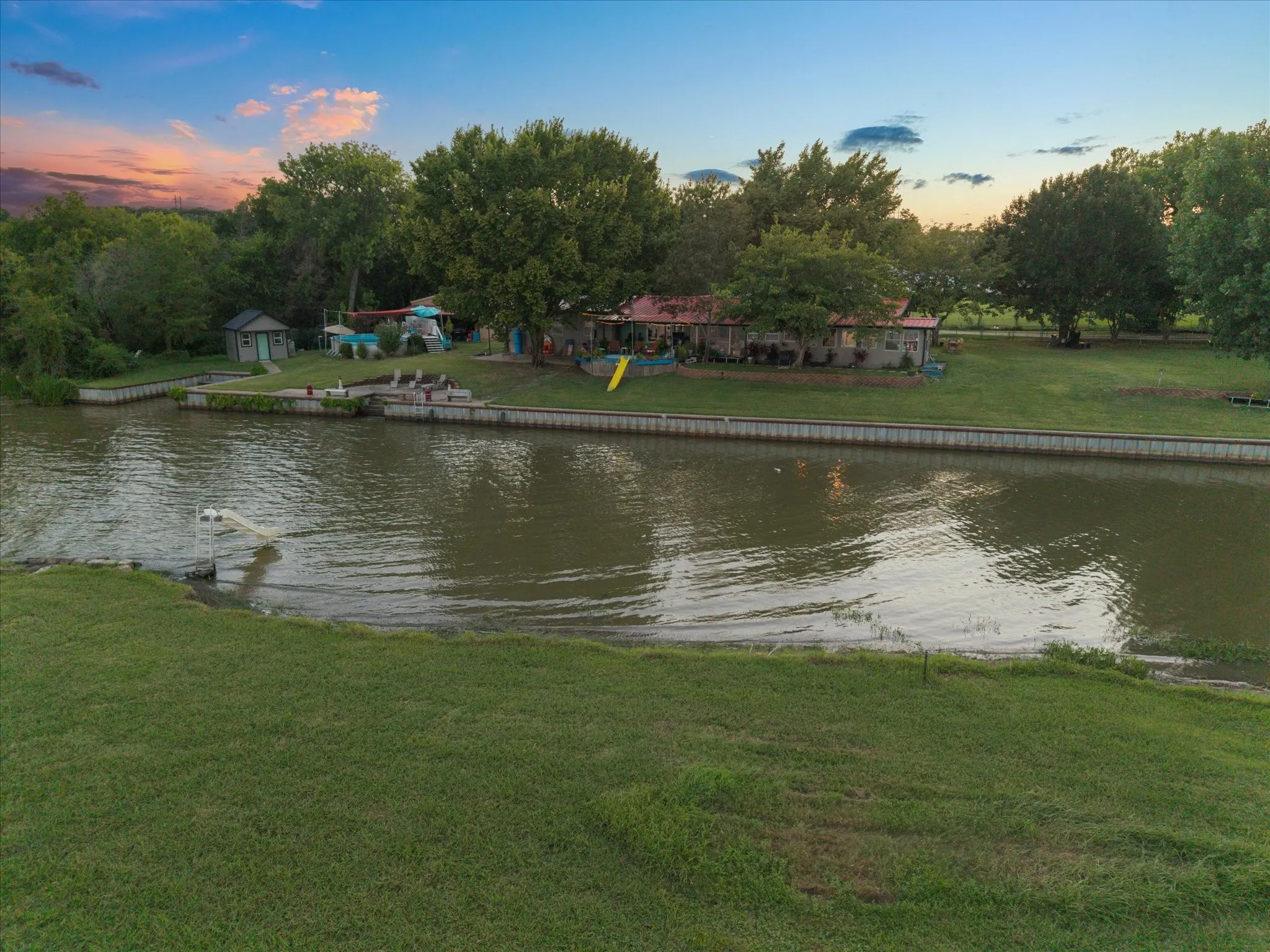 Waterfront property featuring a detached shed, dock with ladder, and expansive green lawn