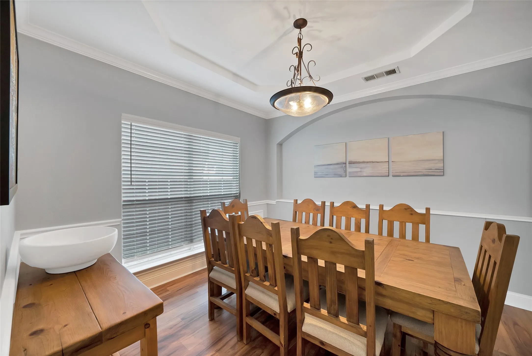 Tray ceiling with a decorative light fixture, wood-finish flooring, and crown molding