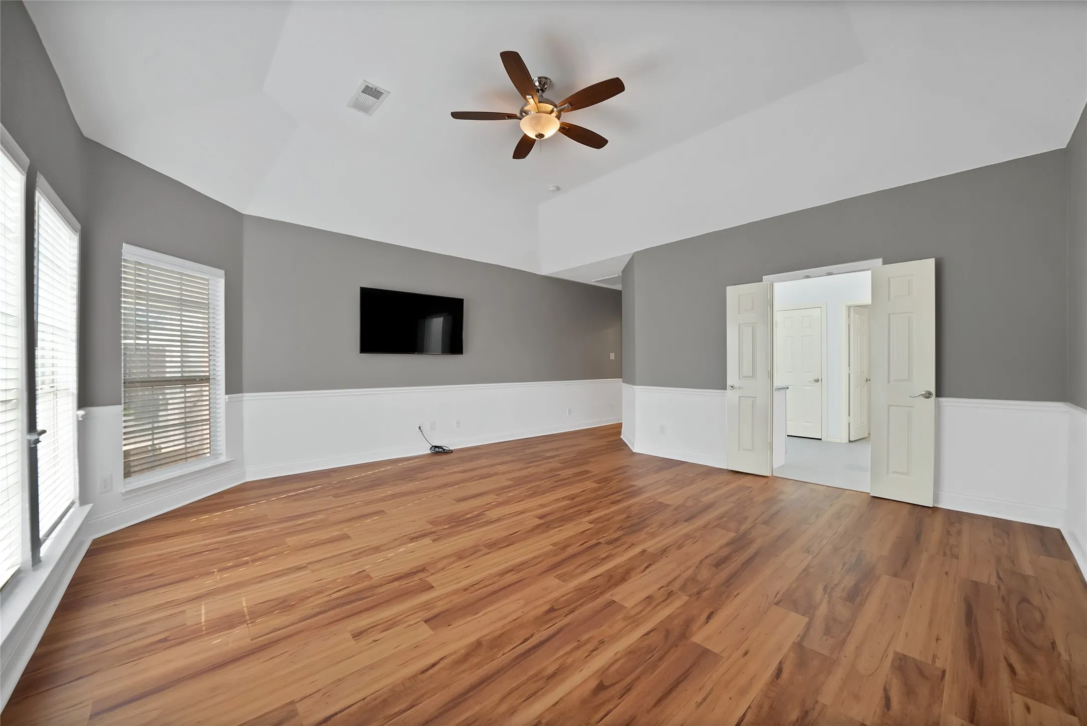 Wood-finish flooring, vaulted ceiling, ceiling fan, two-tone wall treatment, and white paneled doors