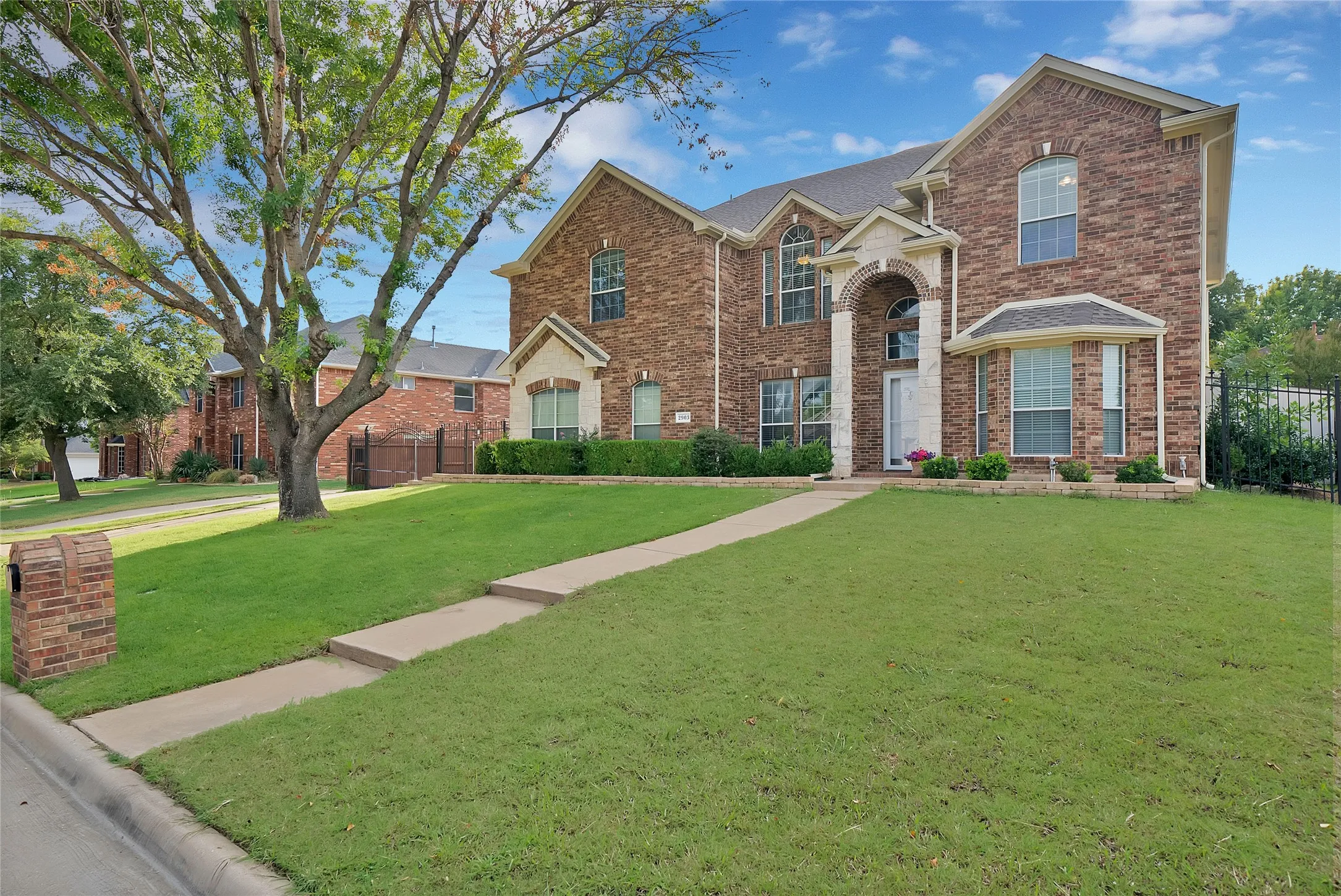 Brick and stone exterior with arched entryway, bay windows, and manicured lawn