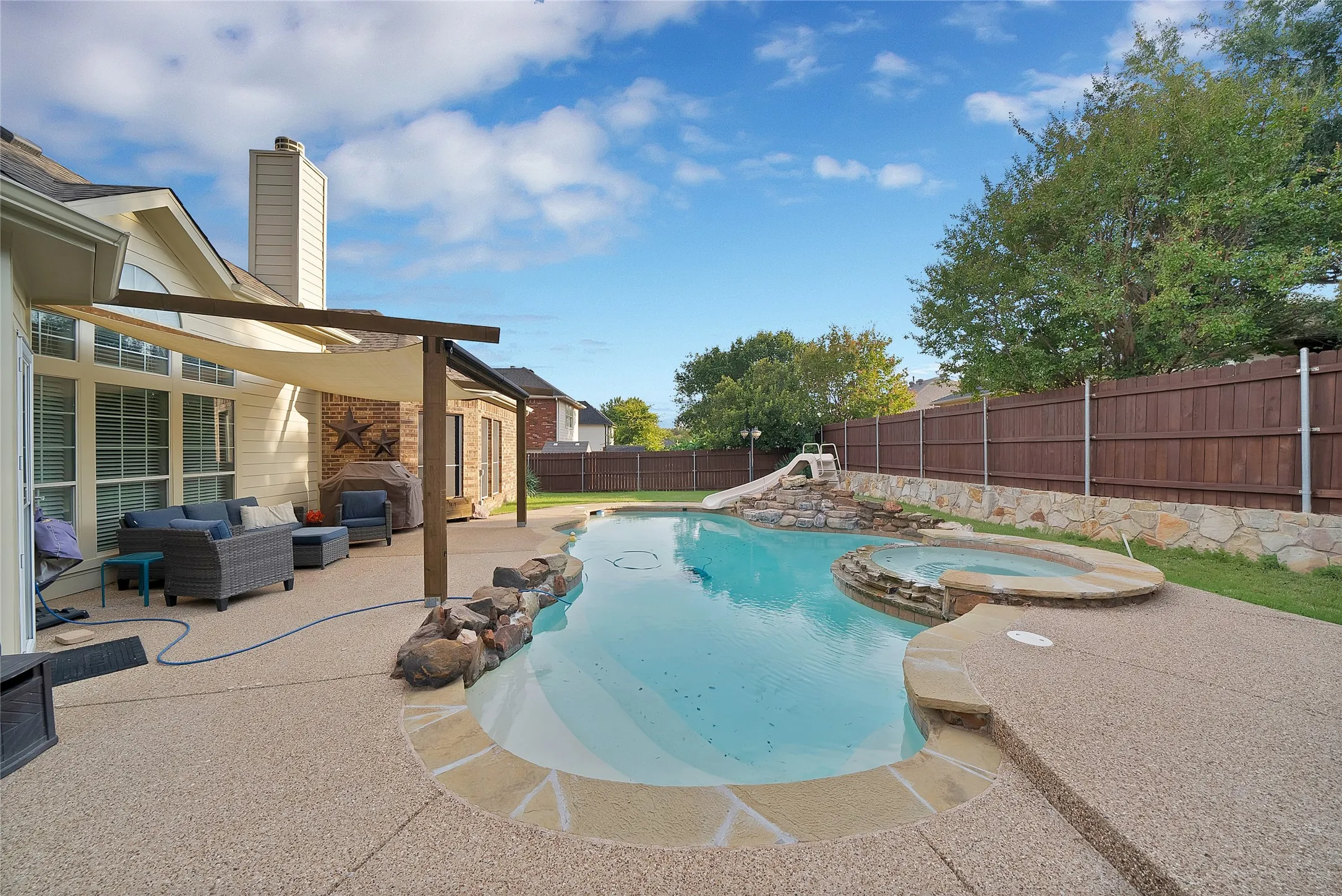 Expansive outdoor living area featuring a custom-shaped swimming pool with an integrated spa, a built-in pool slide, and a covered patio with a shade sail