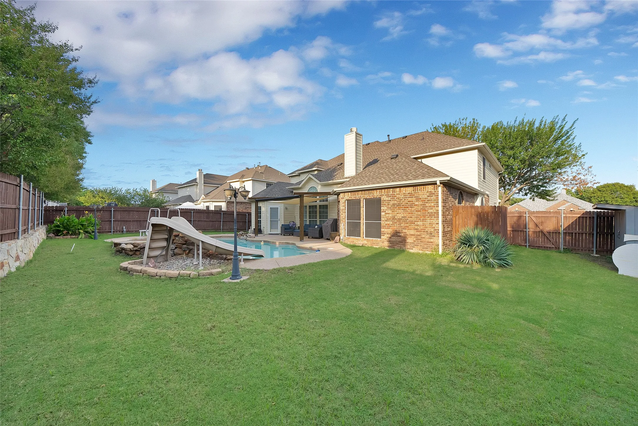 Expansive backyard featuring a manicured lawn, a swimming pool with a slide, and a covered patio area