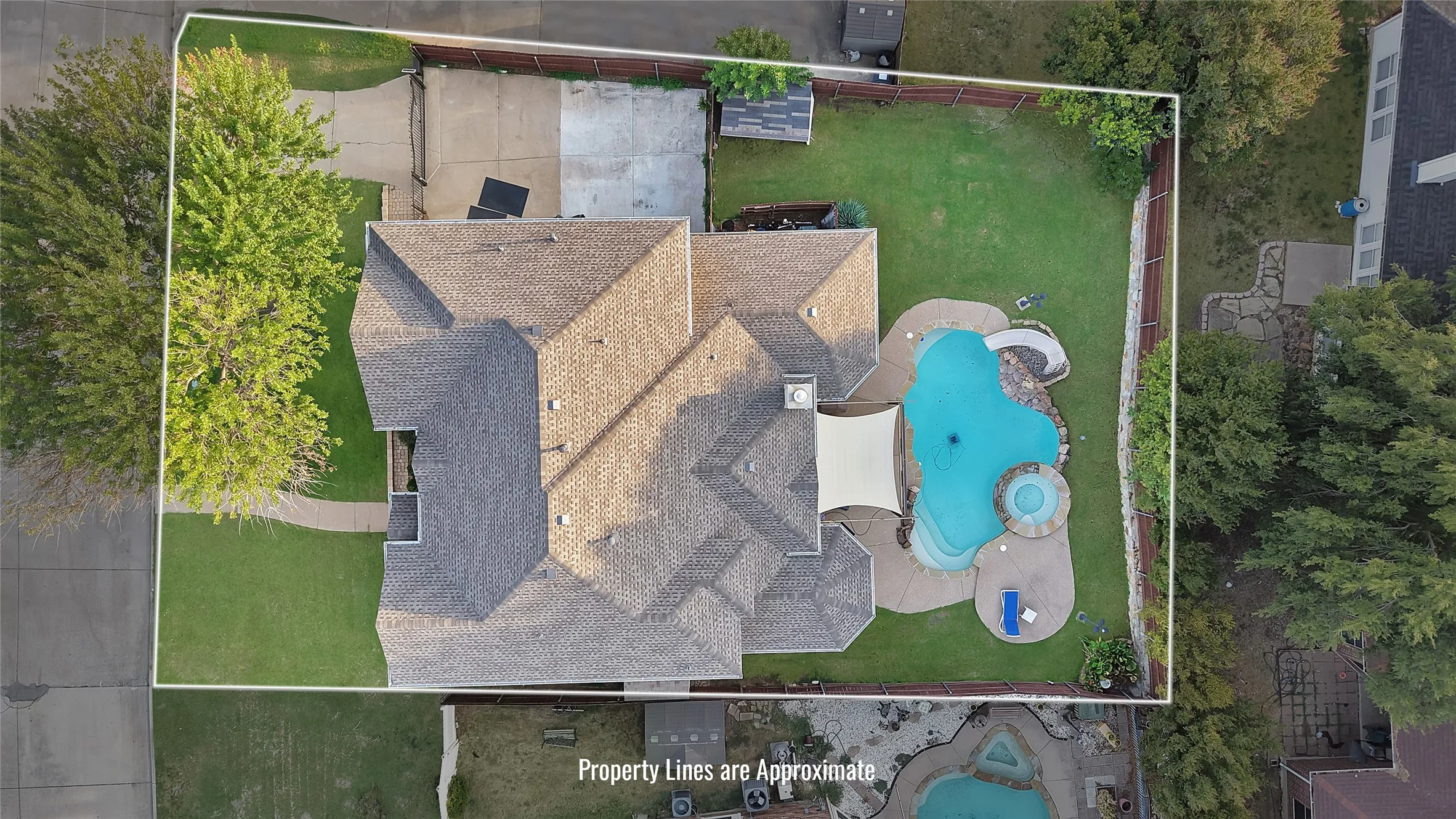 Irregular-shaped swimming pool with an integrated spa, extensive surrounding hardscaping, and a shaded patio area