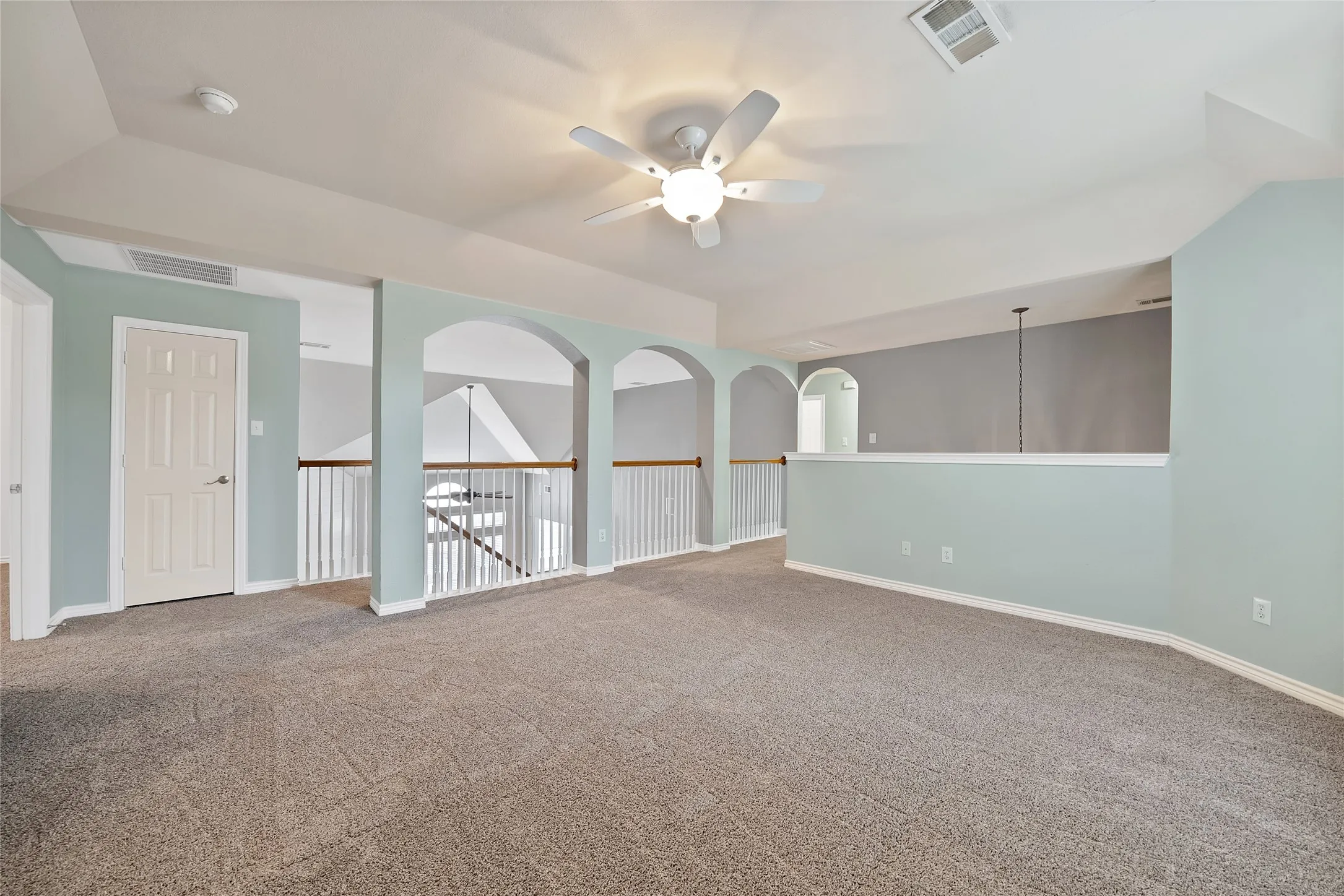 Carpeted loft area featuring arched openings, a ceiling fan, and painted walls