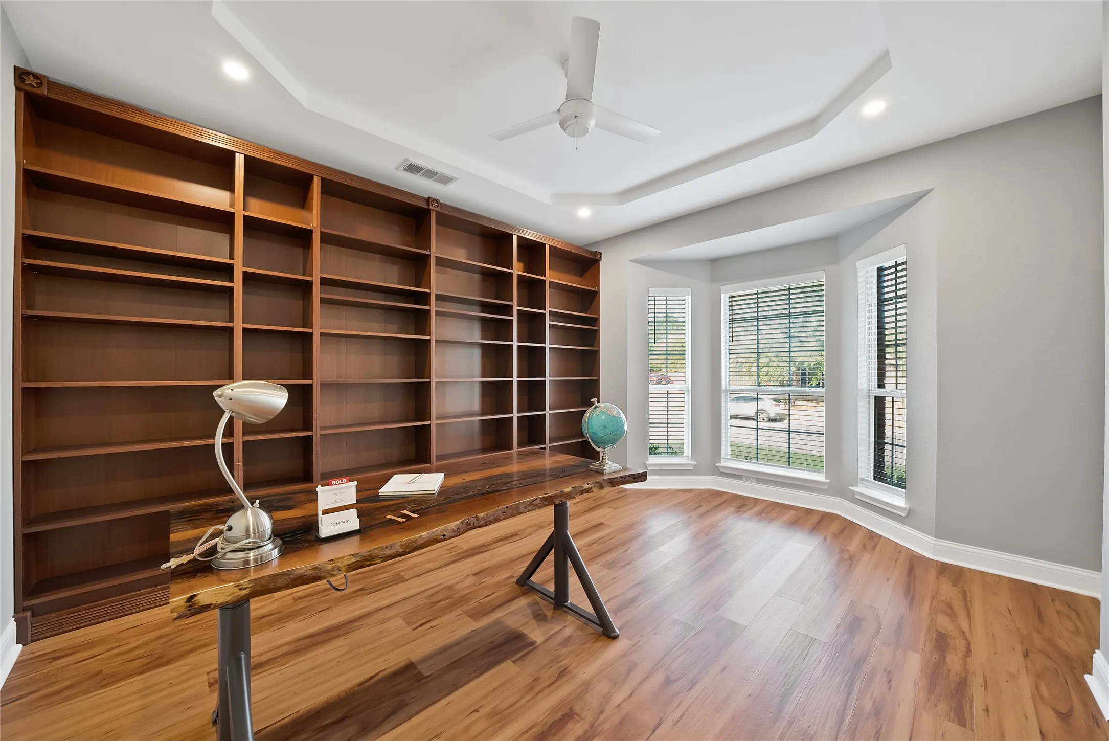Wood-finish flooring, built-in shelving, tray ceiling, recessed lighting, and bay windows