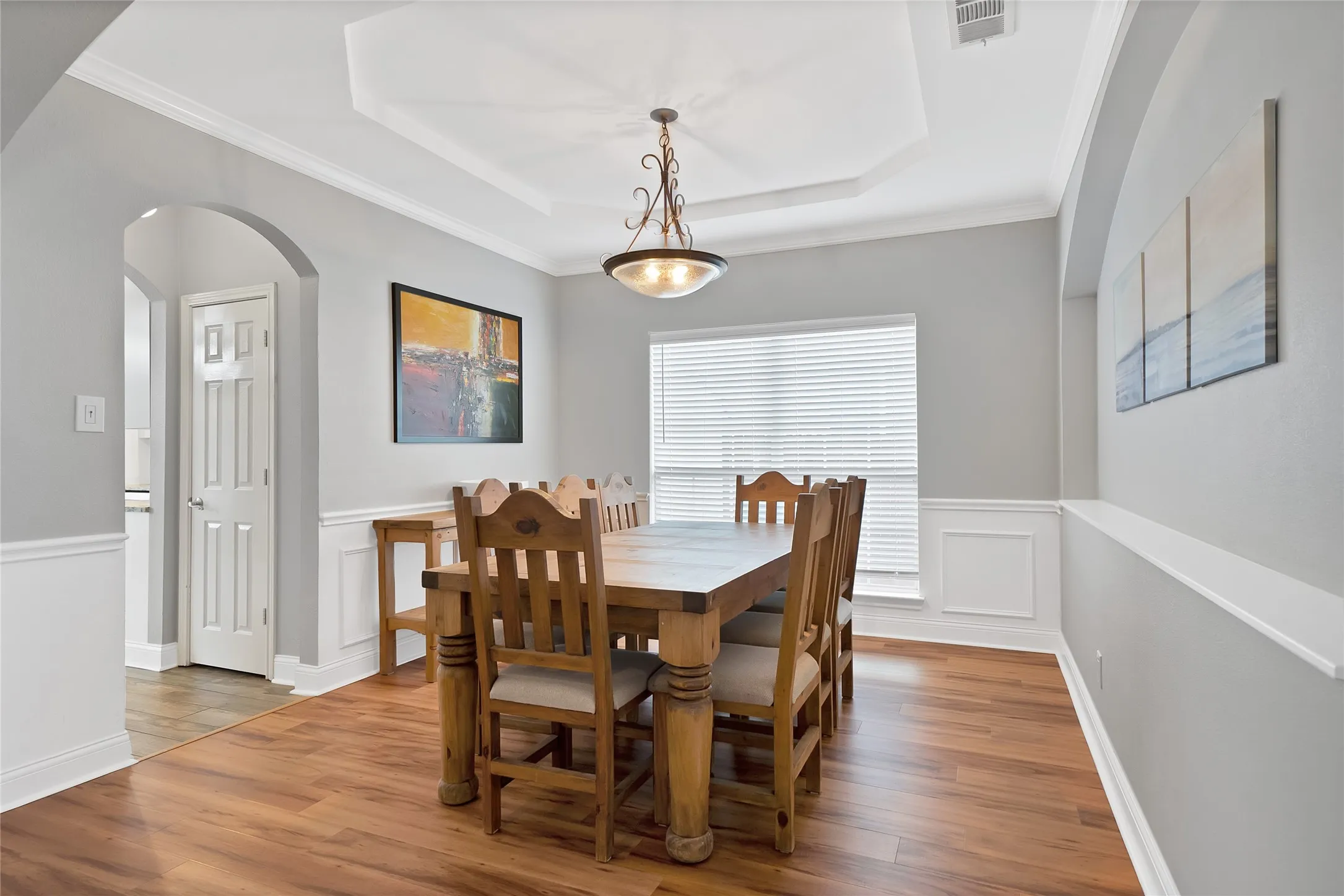 Tray ceiling with an overhead light fixture, wood-finish flooring, wainscoting, and an arched doorway