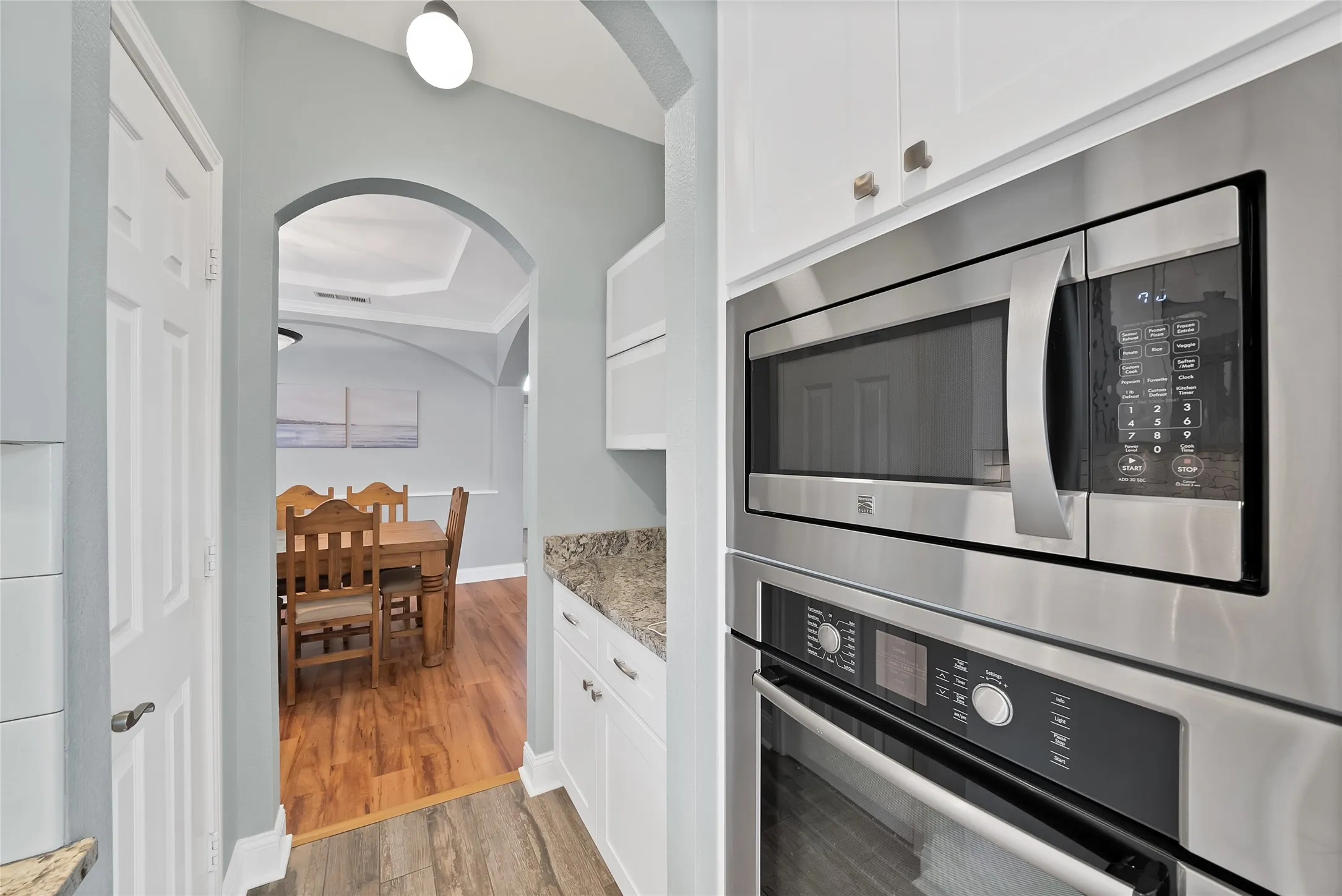 Built-in stainless steel microwave and oven, white cabinetry, and granite-style countertop
