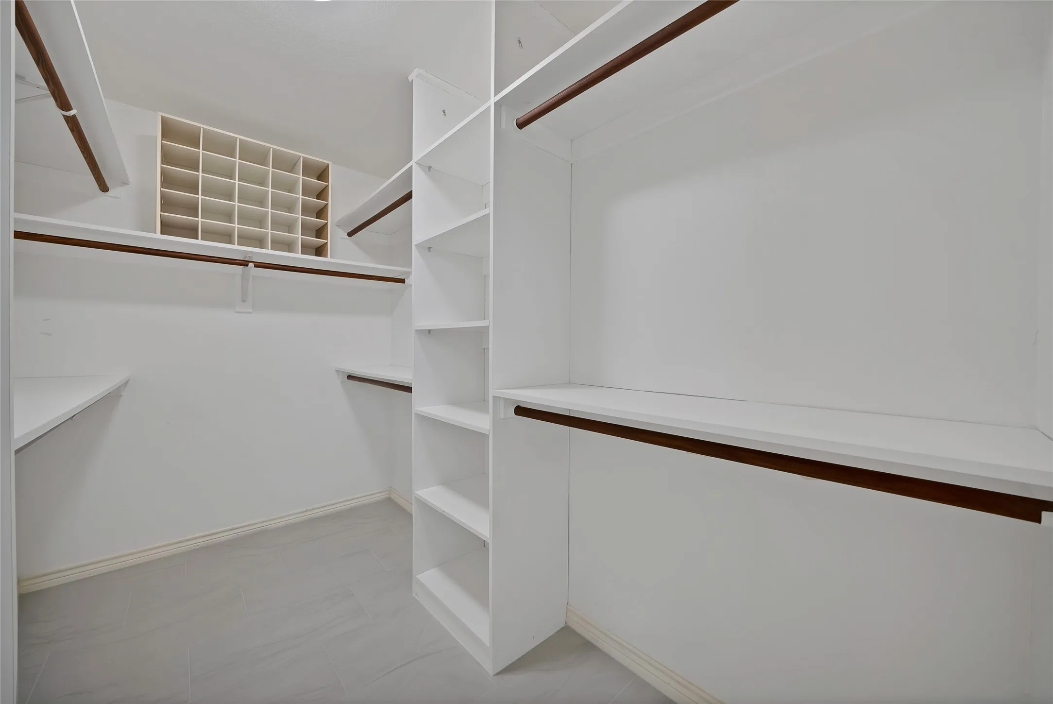 Custom closet organization system featuring white shelving, multiple hanging rods, and an integrated shoe cubby