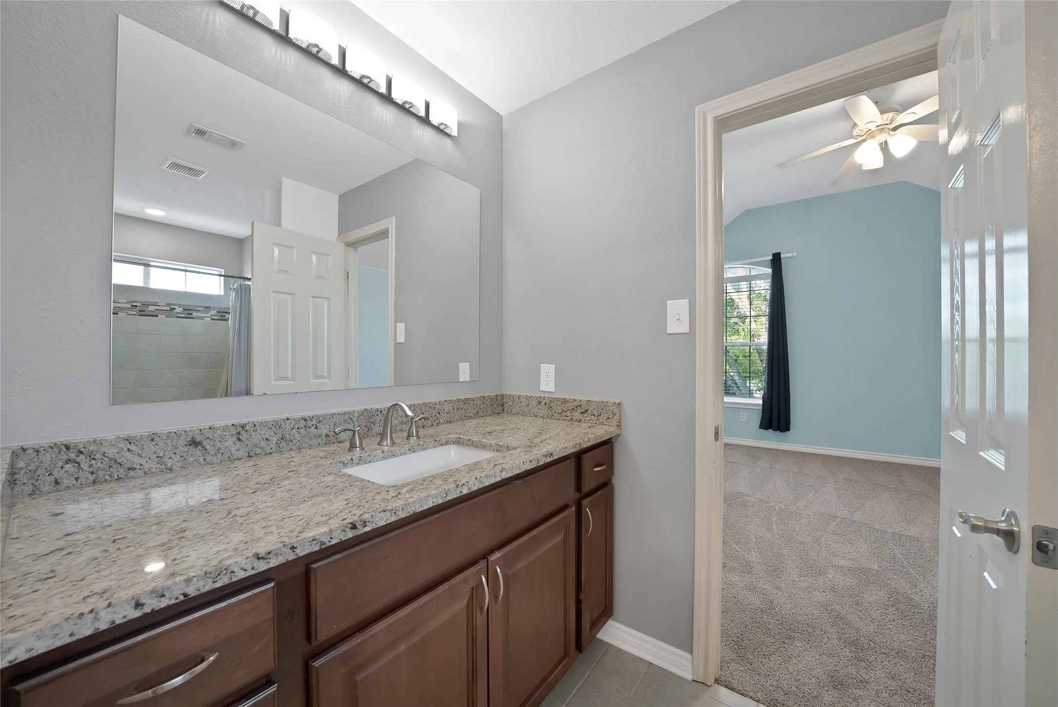 Granite-style countertop with undermount sink, brown wood-finish cabinetry, and framed mirror with overhead vanity lighting