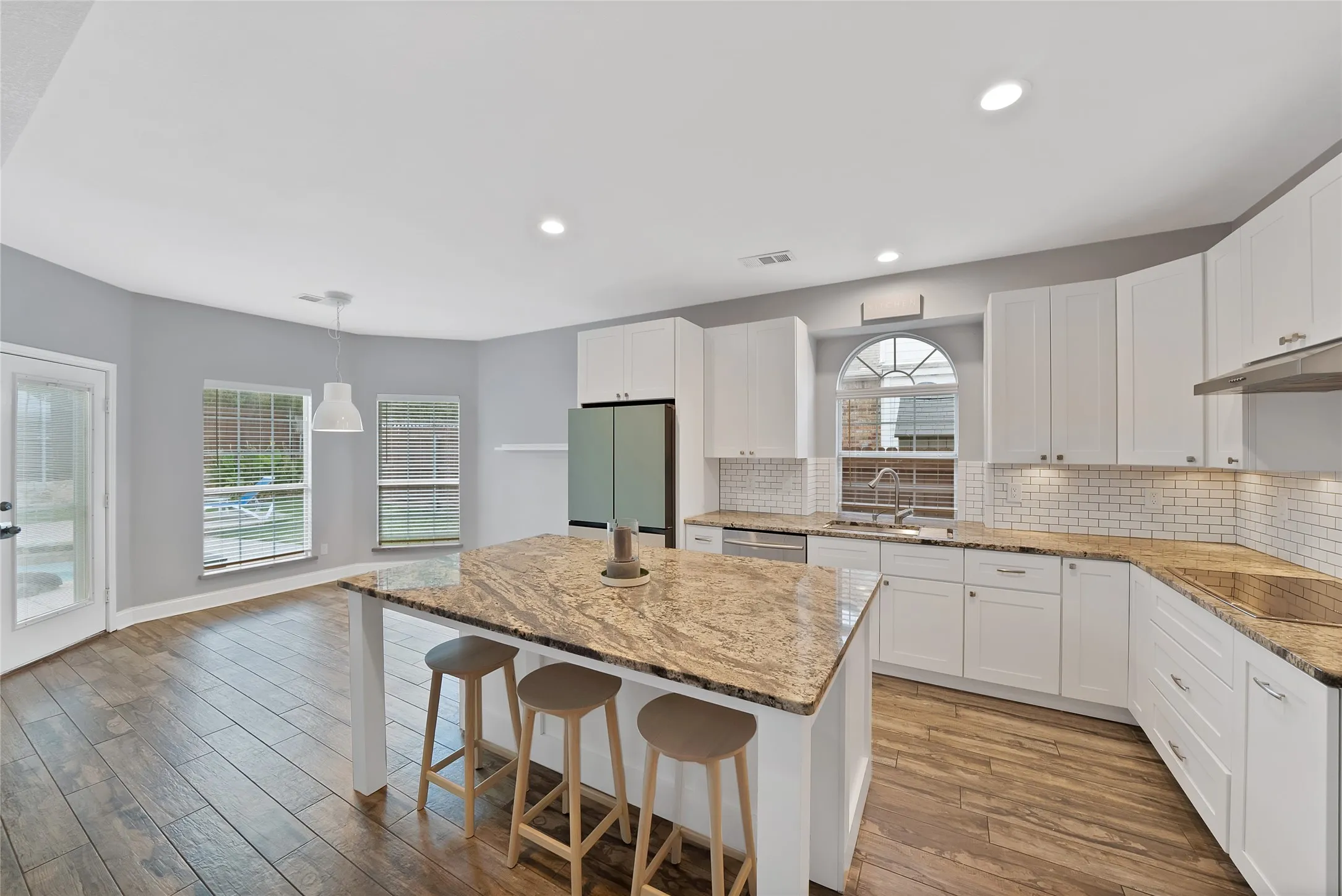 Kitchen featuring wood-finish flooring, white cabinetry, granite countertops, and a subway tile backsplash