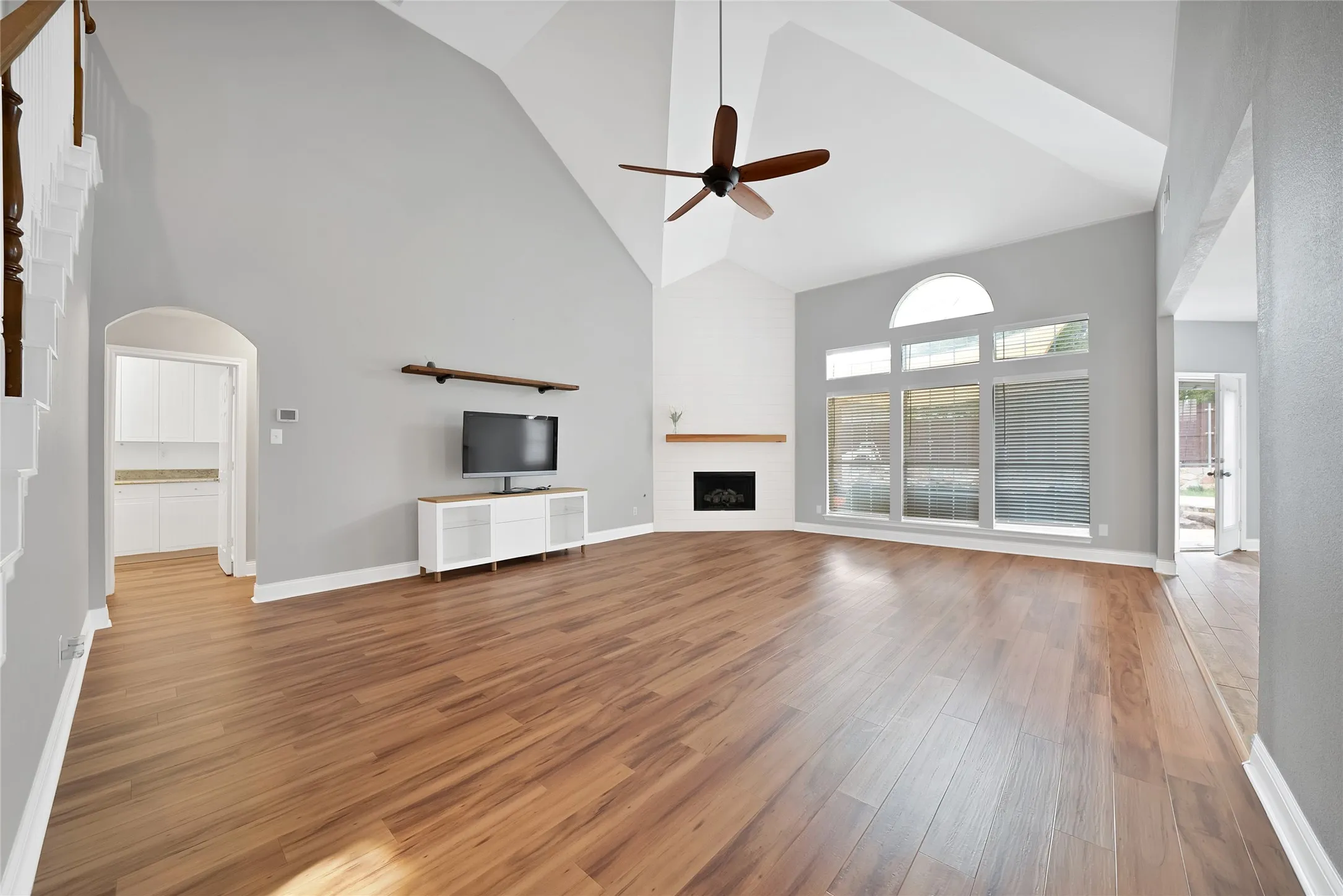Vaulted ceiling with a ceiling fan, wood-finish flooring, fireplace with wood mantel, arched window, and French doors