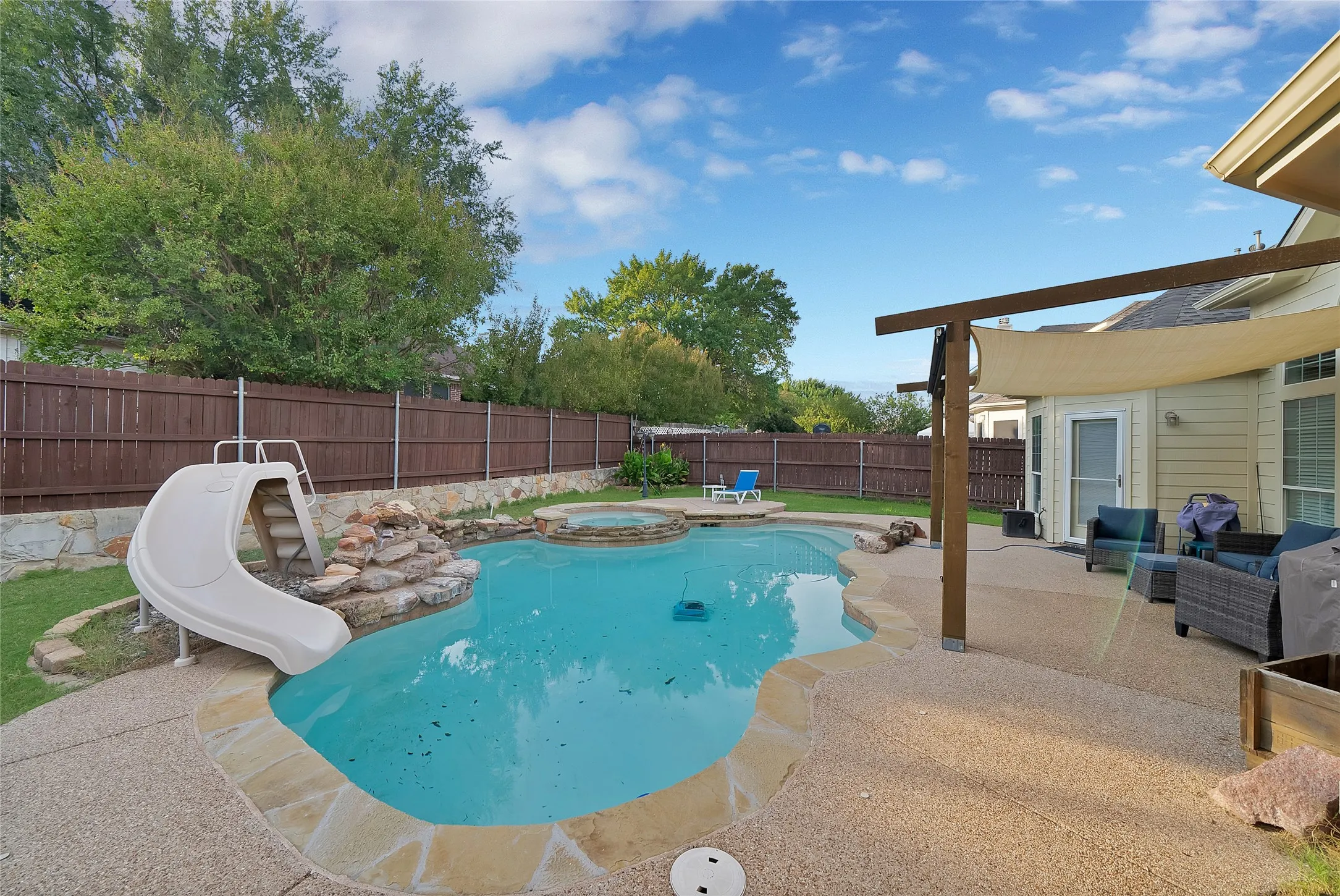 Outdoor pool with a stone waterfall feature, integrated spa, and an attached slide