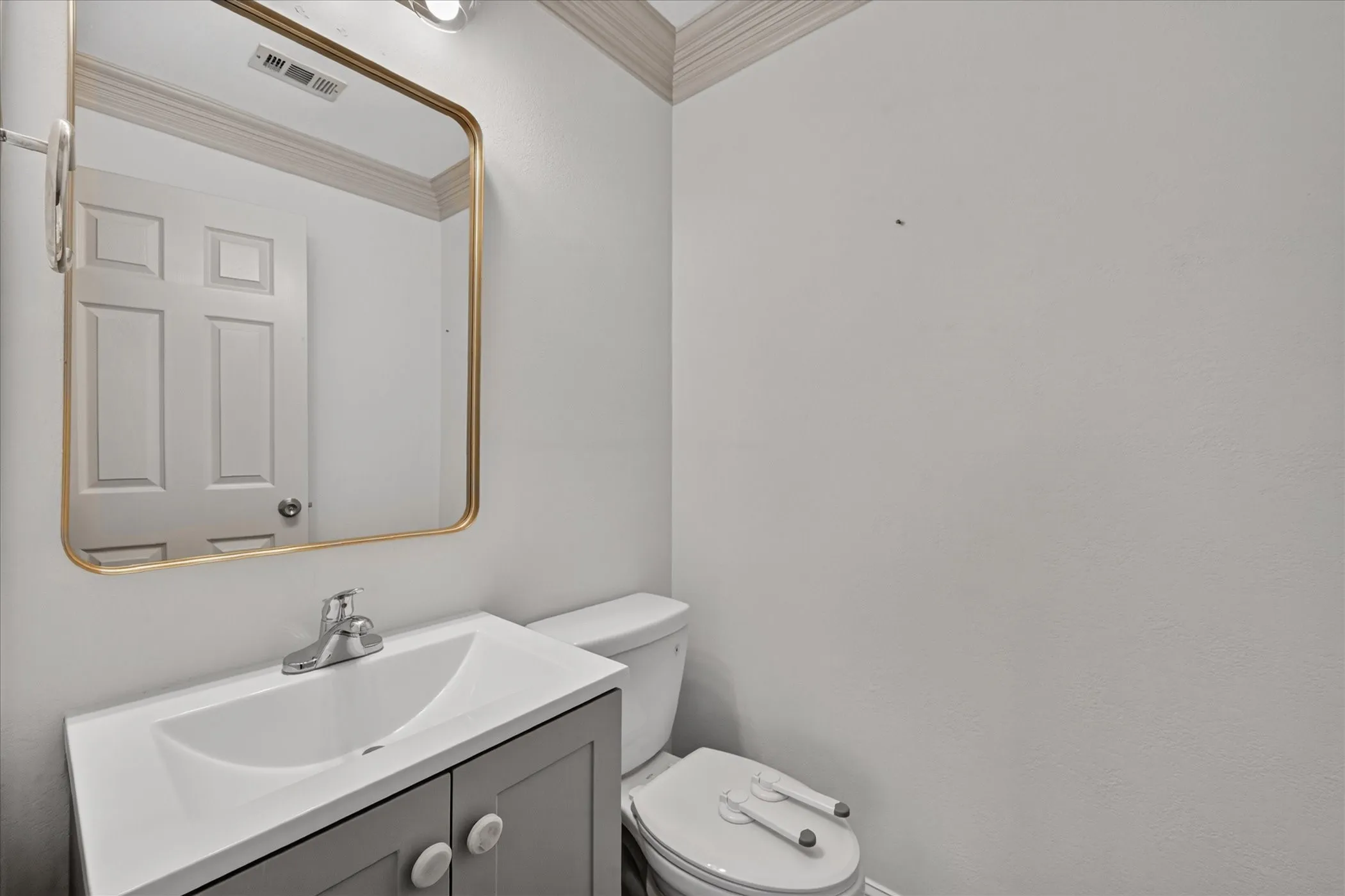 Vanity with an integrated sink, polished chrome faucet, rectangular gold-framed mirror, and a toilet
