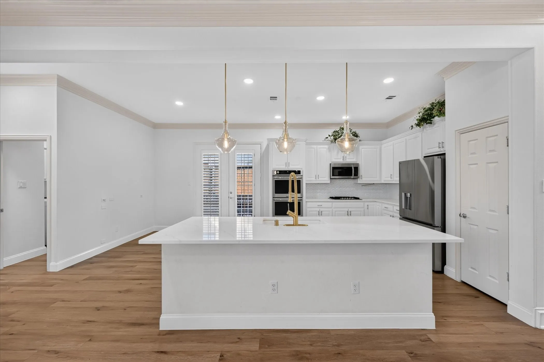 Gourmet kitchen featuring a large island with white stone countertop, white cabinetry, integrated stainless steel appliances, and wood-finish flooring