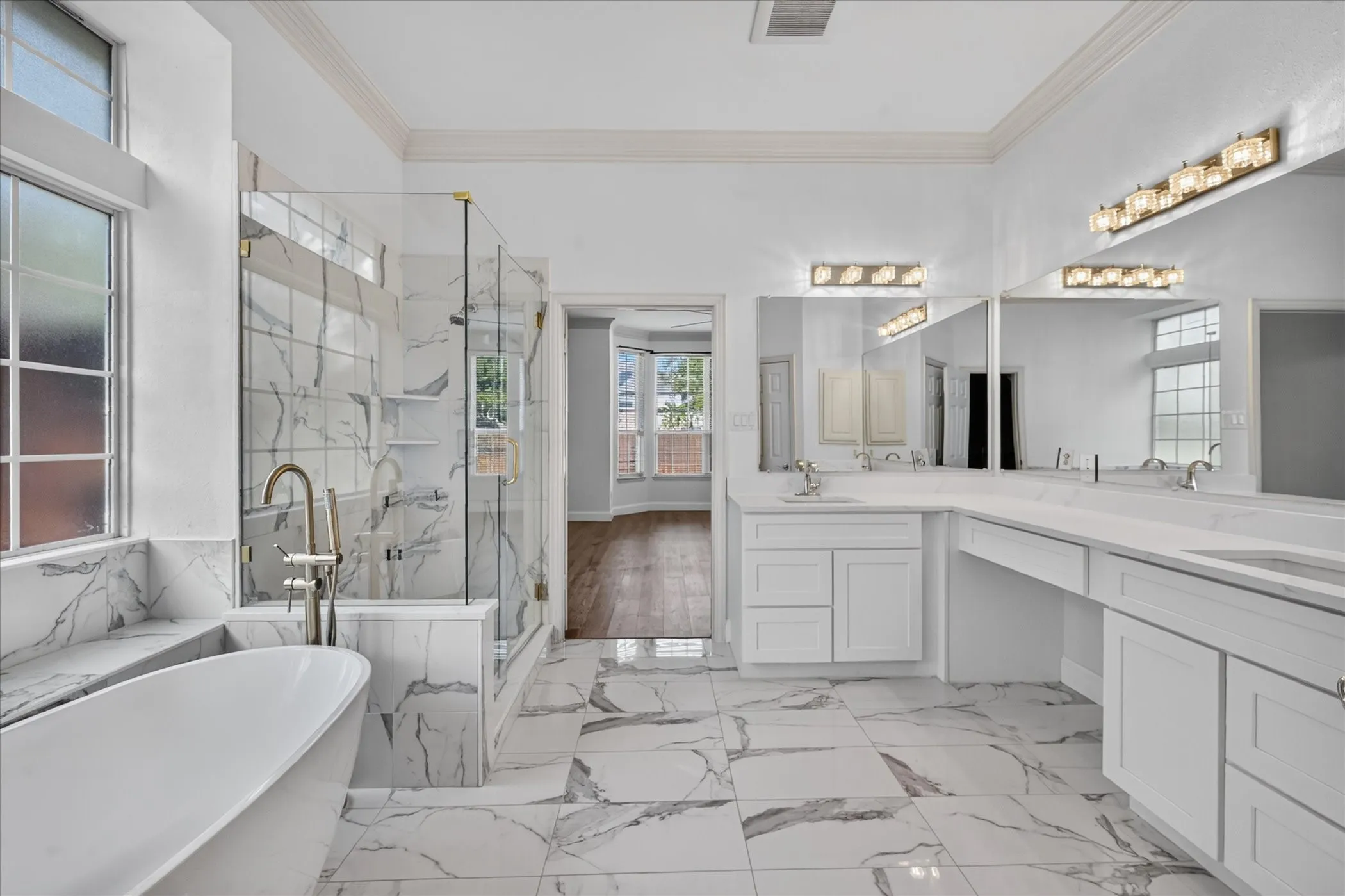 Freestanding soaking tub, walk-in shower with clear glass enclosure, dual vanity sinks, and expansive vanity mirrors
