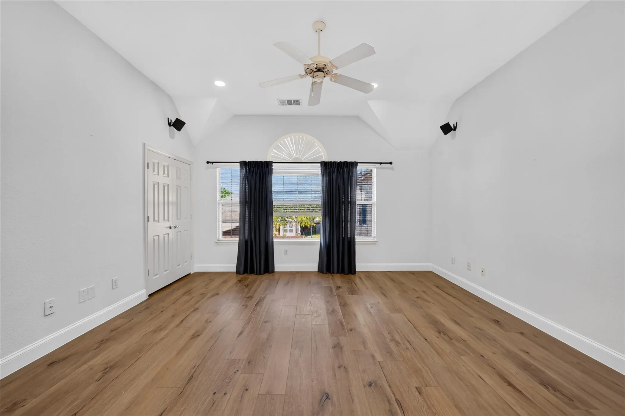 Vaulted ceiling with a ceiling fan, recessed lighting, wood-finish flooring, and a window with an arched transom
