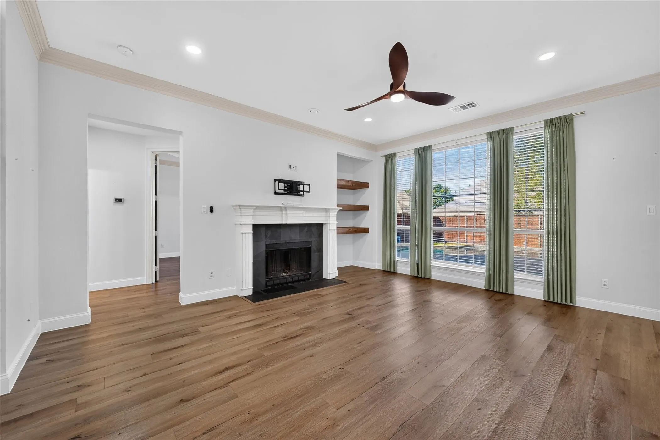 Wood-finish flooring, recessed lighting, and a fireplace with a dark stone surround