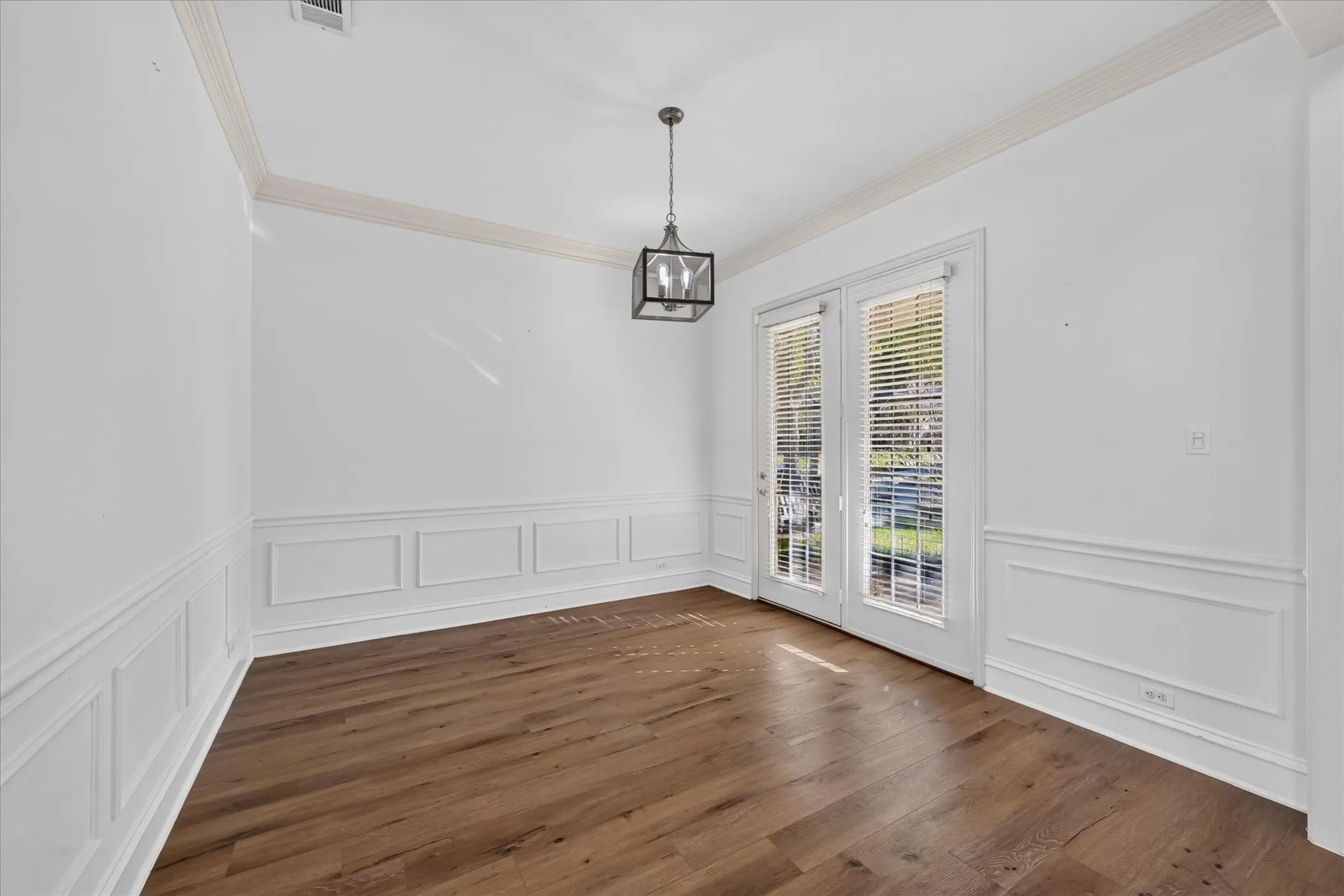 Wood-finish flooring, crown molding, wainscoting, double glass-paned doors, and a contemporary ceiling fixture
